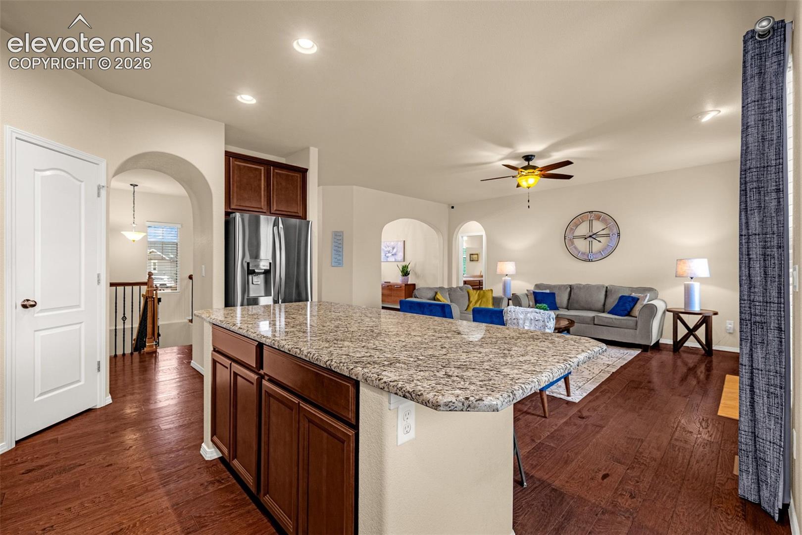 Kitchen island with stone countertop and wood-finish cabinetry, stainless steel refrigerator, recessed lighting, and wood-finish flooring throughout