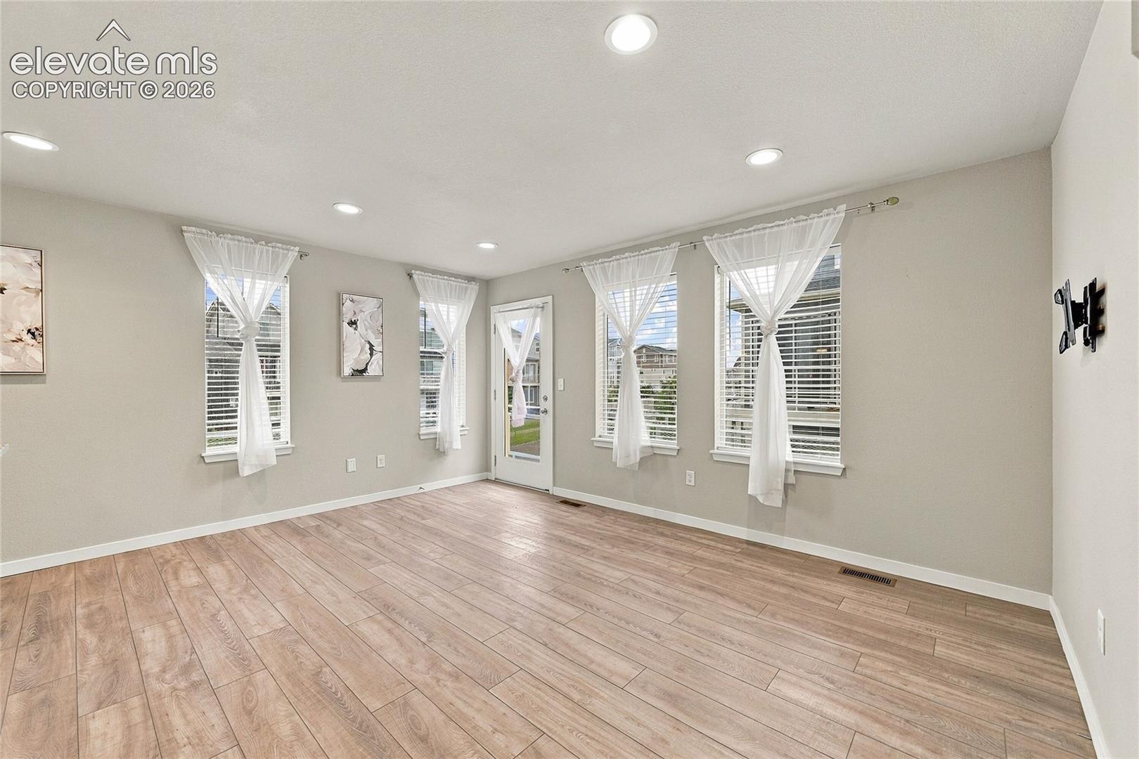 Recessed lighting, wood-finish flooring, multiple windows, and a rear door with a full-light inset