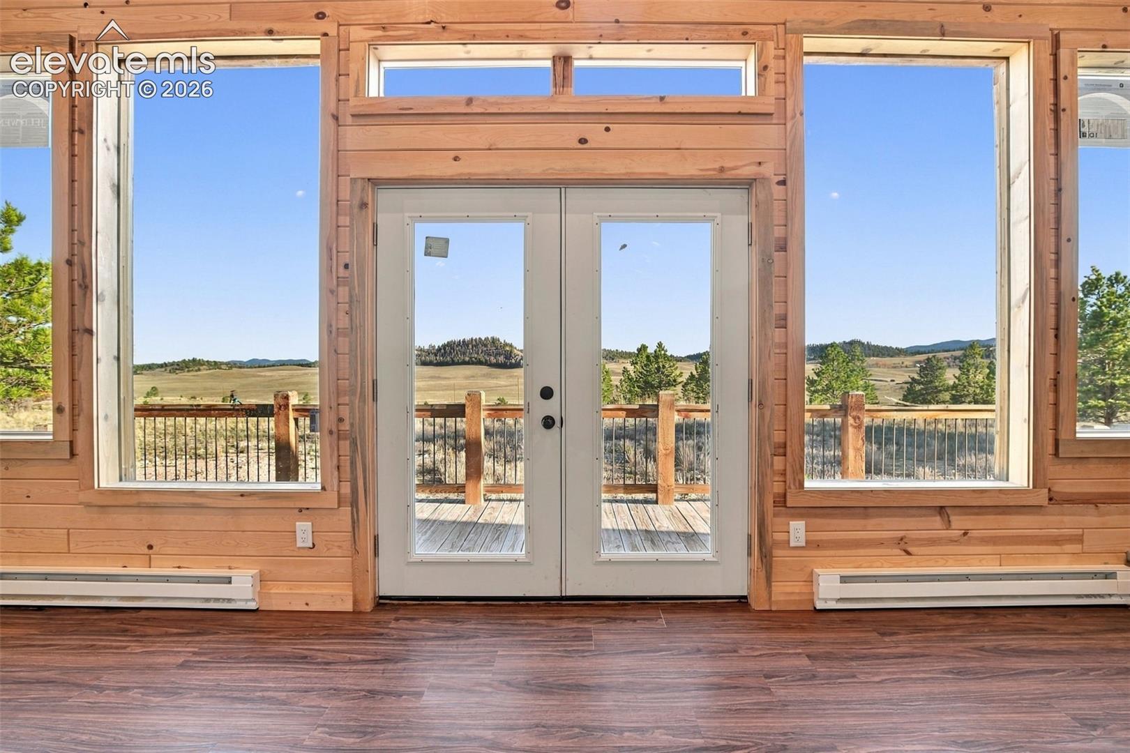 Natural wood wall paneling, floor-to-ceiling windows, wood-finish flooring, and double glass-paneled exterior doors with a transom window
