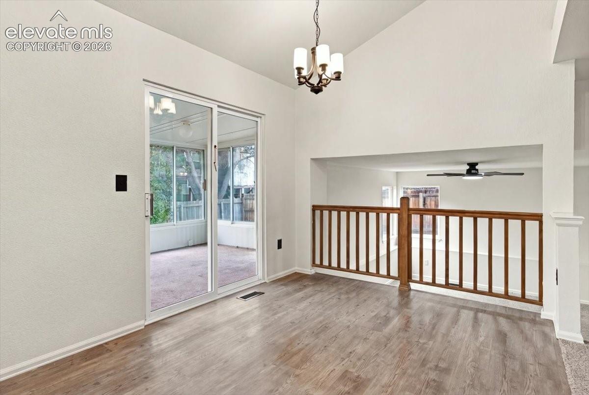 Vaulted ceilings, wood-finish flooring, sliding glass patio door, multi-arm chandelier, and wooden staircase railing