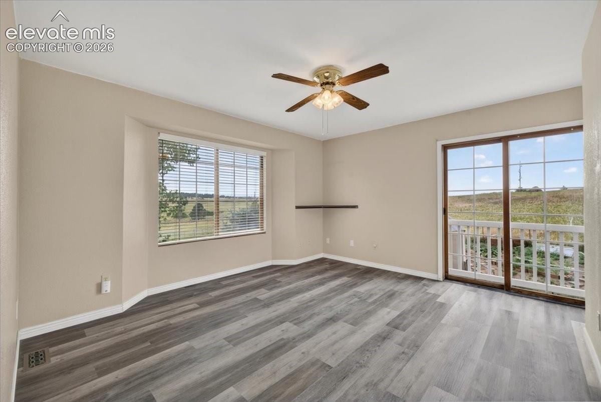 Bedroom or office featuring wood-finish flooring, a ceiling fan with integrated lighting, a bay window with horizontal blinds, and sliding glass doors with a multi-pane grid design