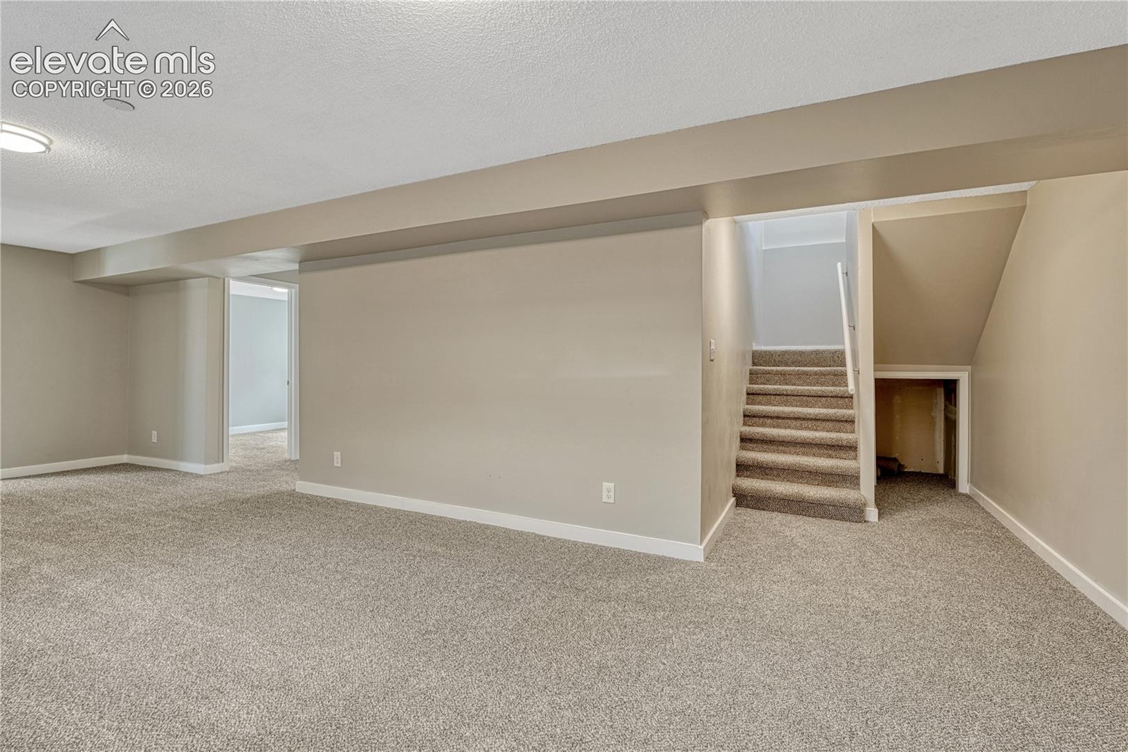 Expansive carpeted area with neutral wall tones and a stairway featuring a carpeted runner