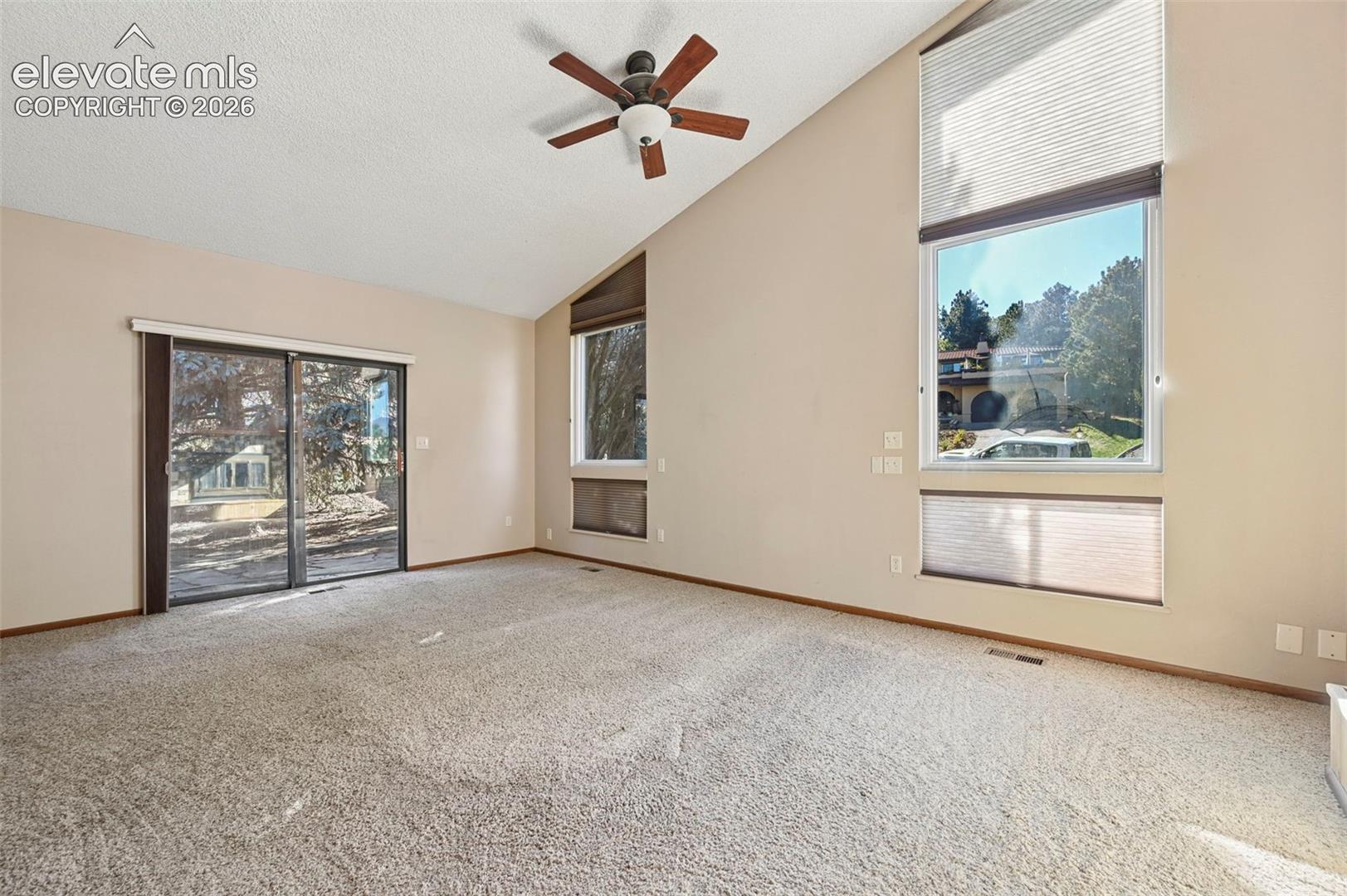 Vaulted ceilings, expansive windows, sliding glass door, and ceiling fan