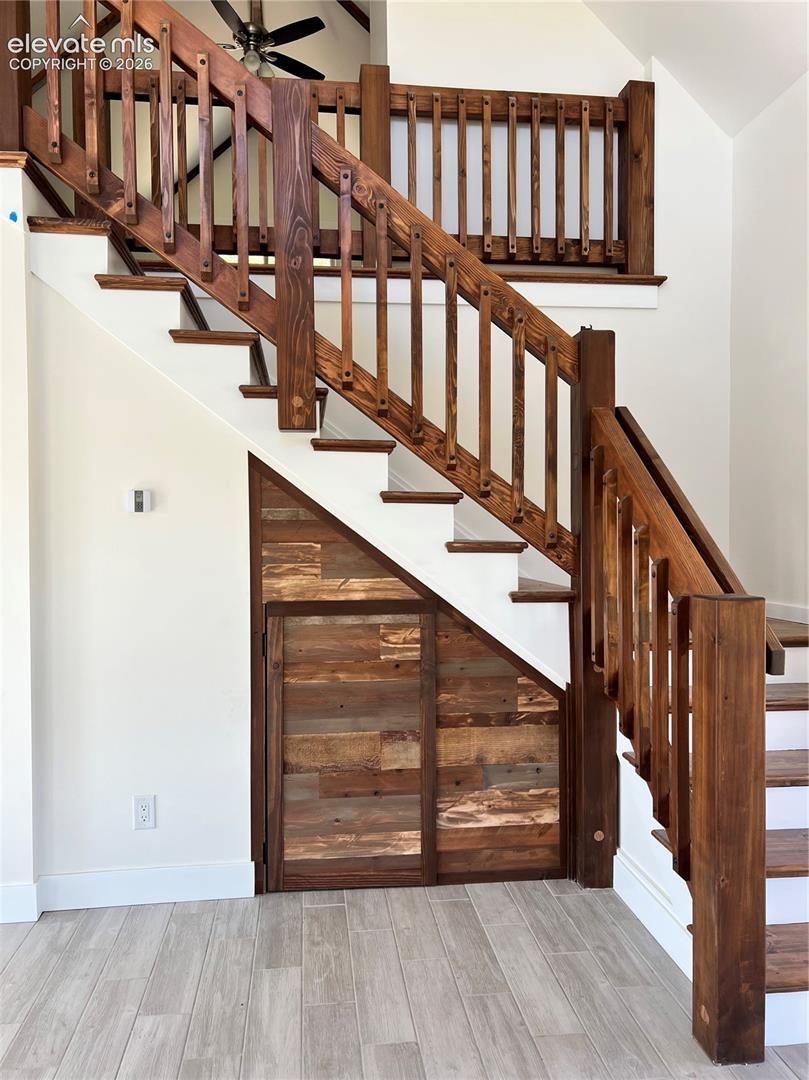 Wood-finish flooring, custom wood staircase with balusters, built-in under-stair storage with horizontal wood paneling, and a high ceiling