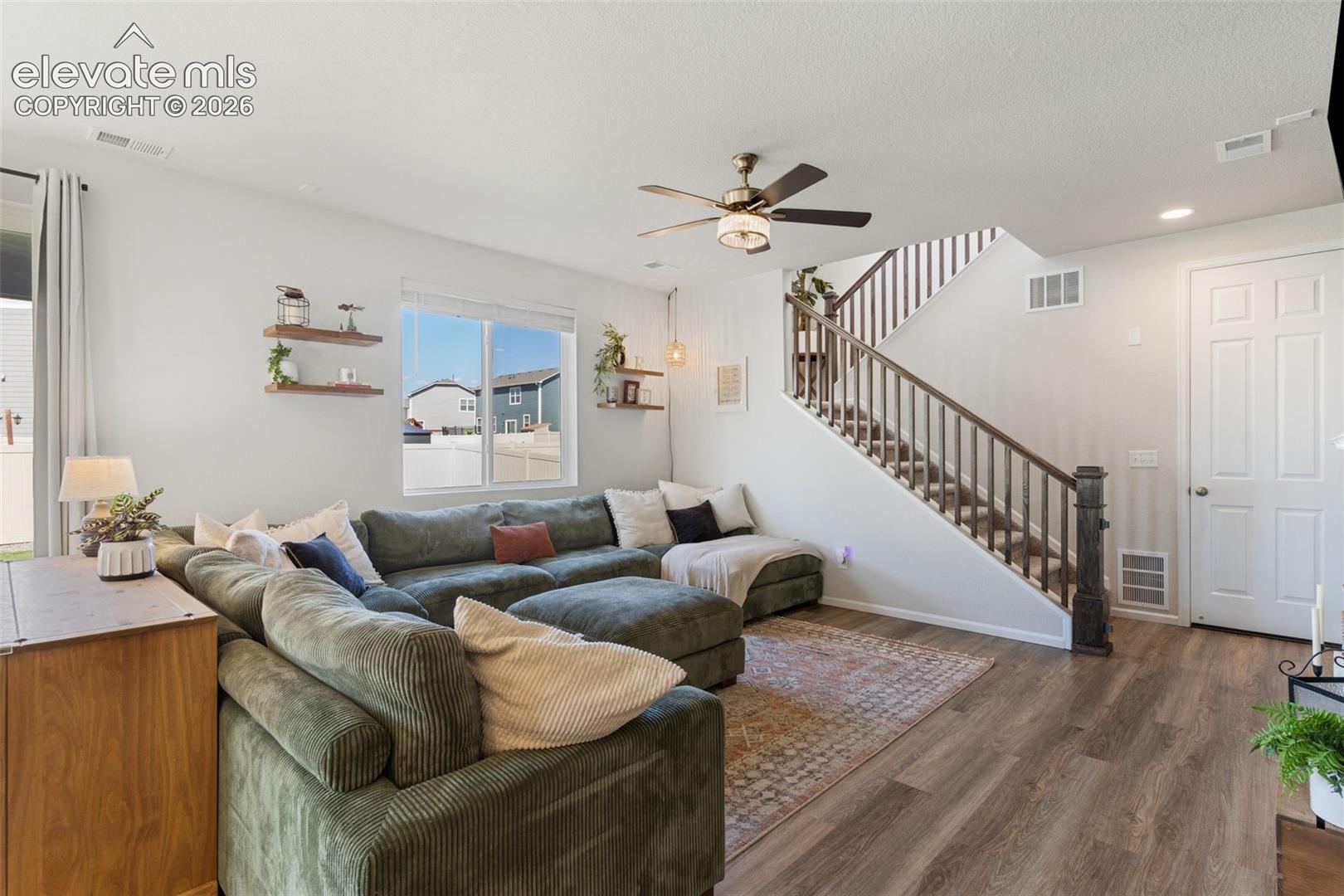 Living area featuring wood-finish flooring, a contemporary ceiling fan, and a staircase with stained wood railings