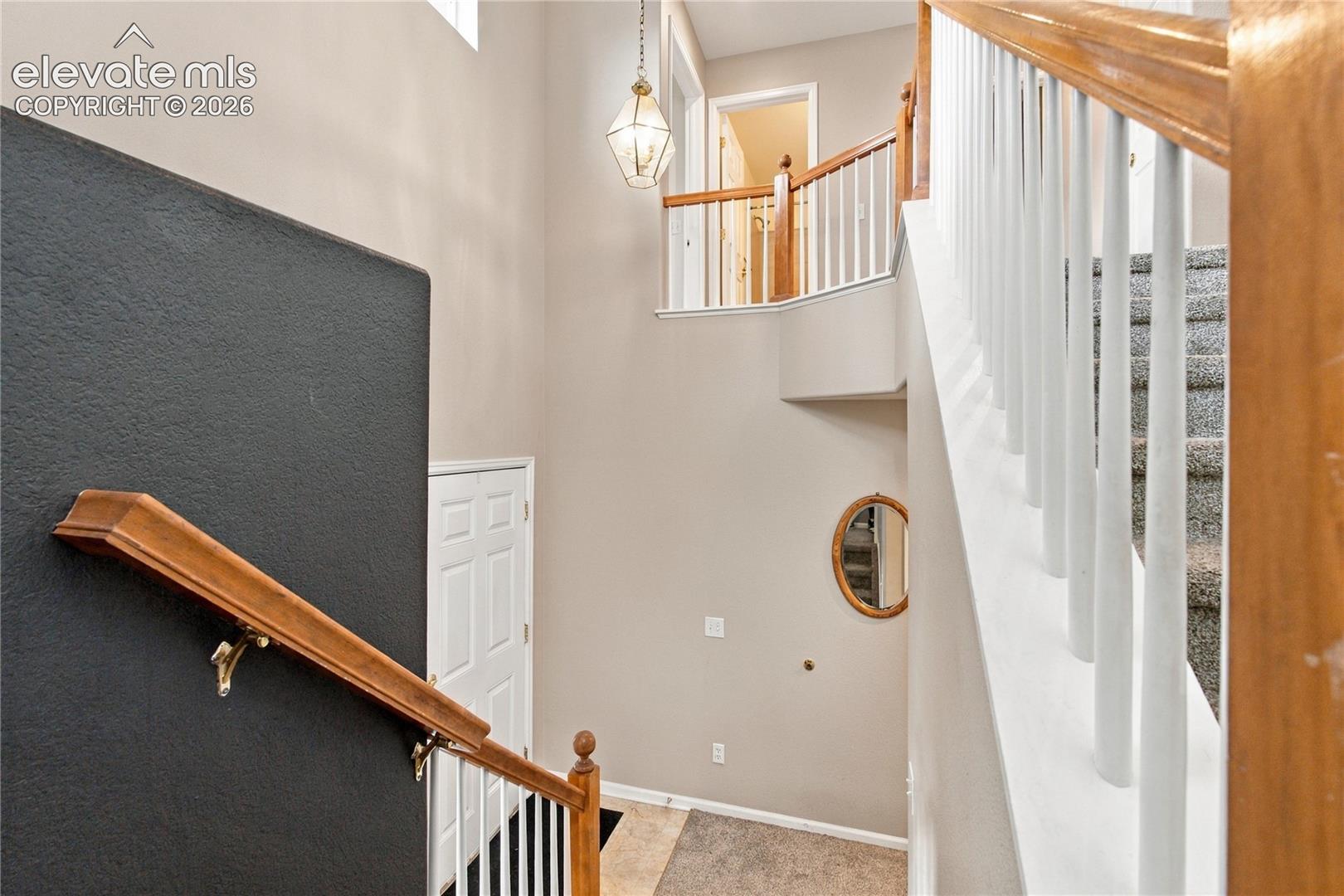 Double-height foyer featuring a staircase with white balusters and wood-finished railings, high ceilings, a geometric pendant light fixture, and tile flooring