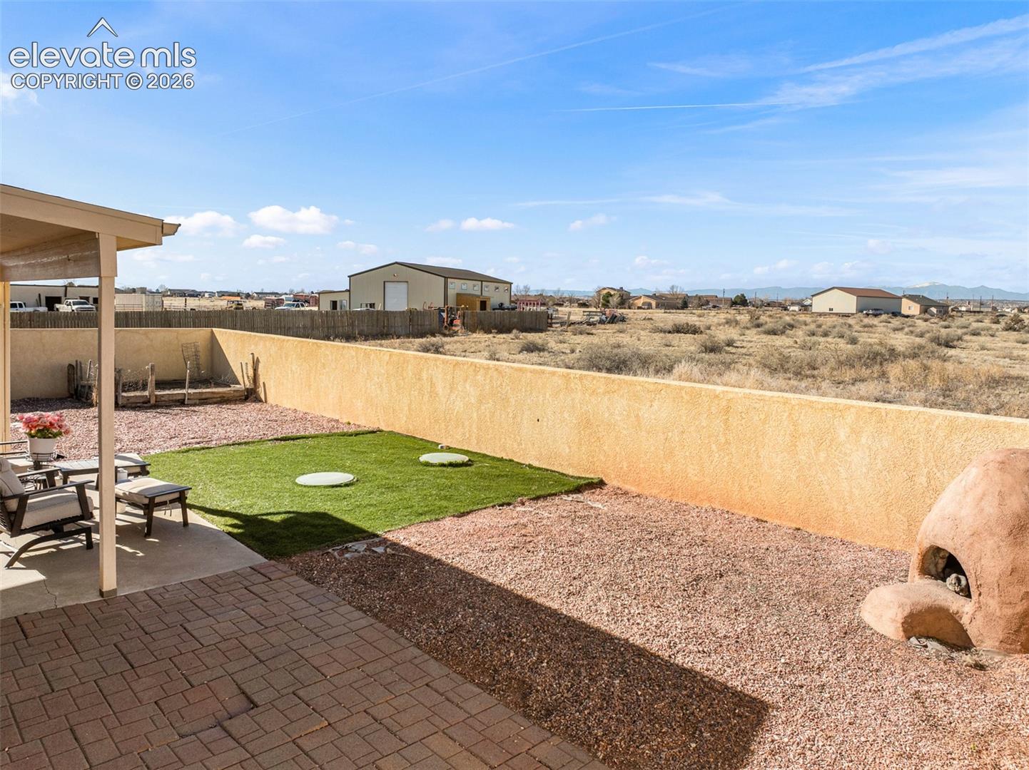 Covered patio with paver flooring, low-maintenance landscaping with gravel and artificial turf, and a built-in outdoor oven