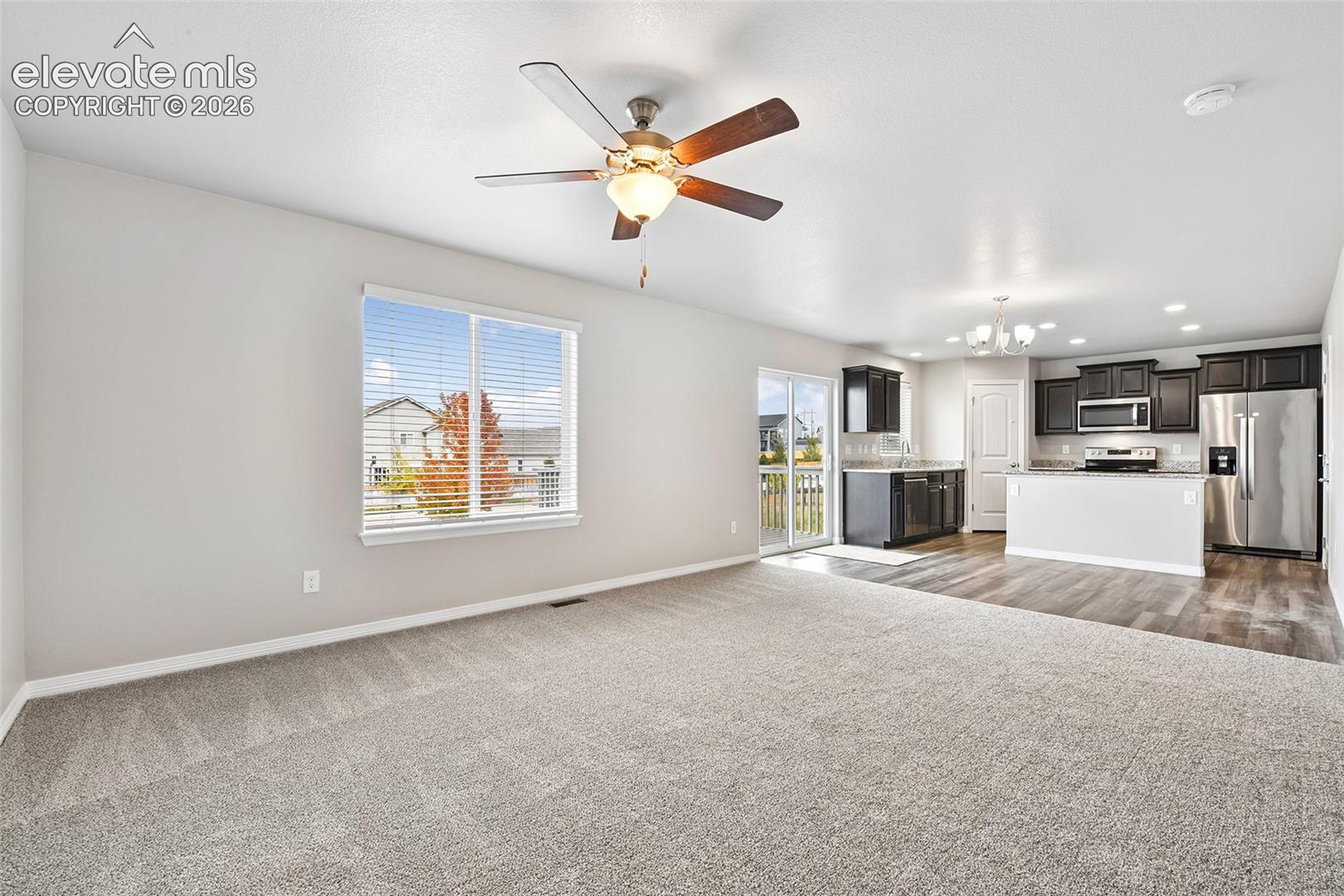Open-concept interior featuring neutral wall-to-wall carpeting, wood-finish flooring, dark-toned cabinetry, stainless steel kitchen appliances, and a ceiling fan with light fixture