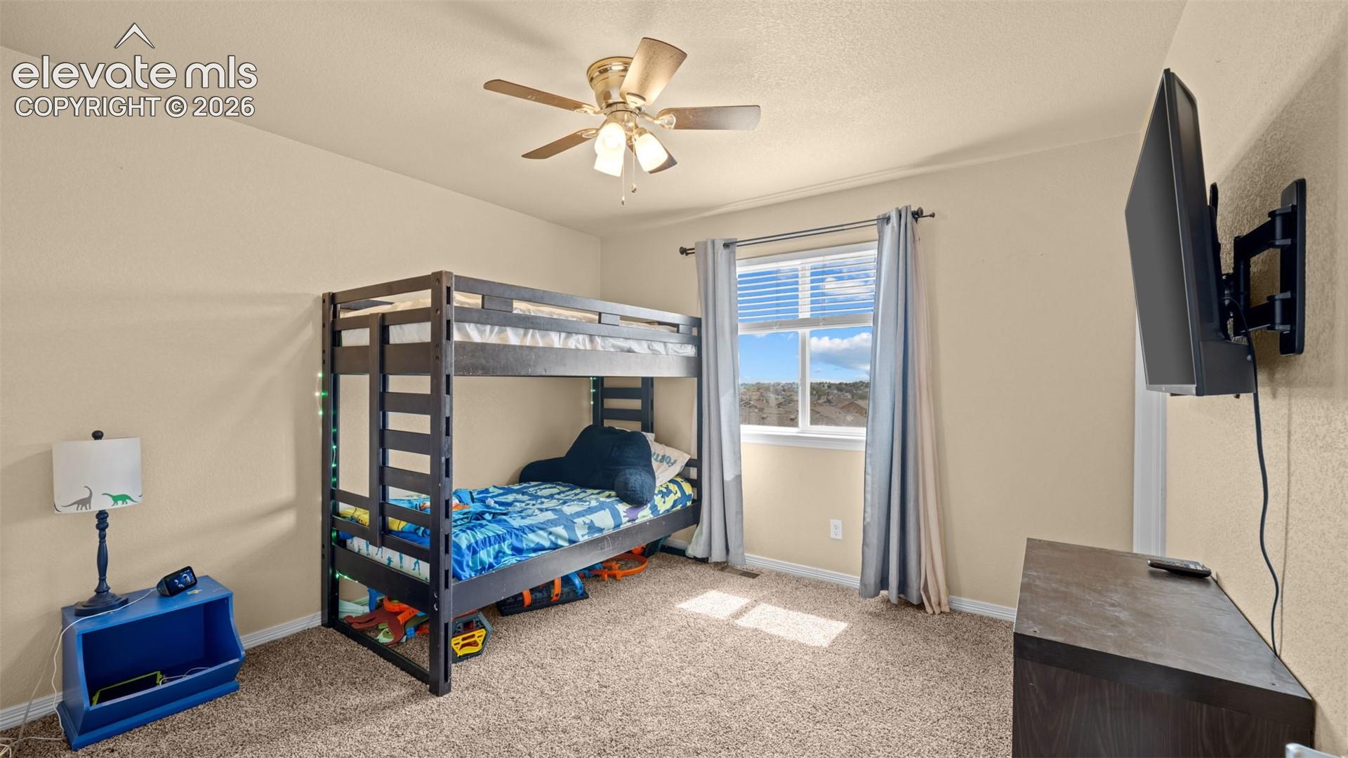 Bedroom featuring light beige wall color, textured carpeting, a window with horizontal blinds and drapery, and a ceiling fan with integrated lighting