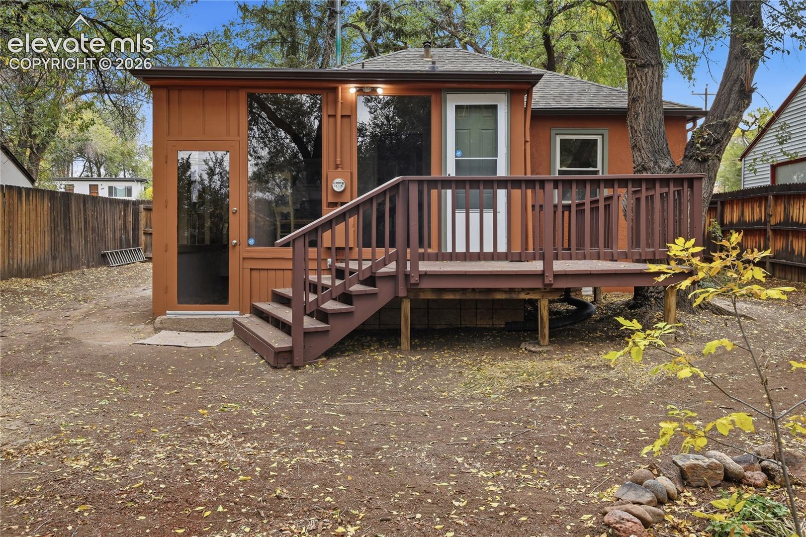Exterior space featuring a raised wooden deck, vertical panel siding, multiple large glass panels, and a surrounding wood privacy fence