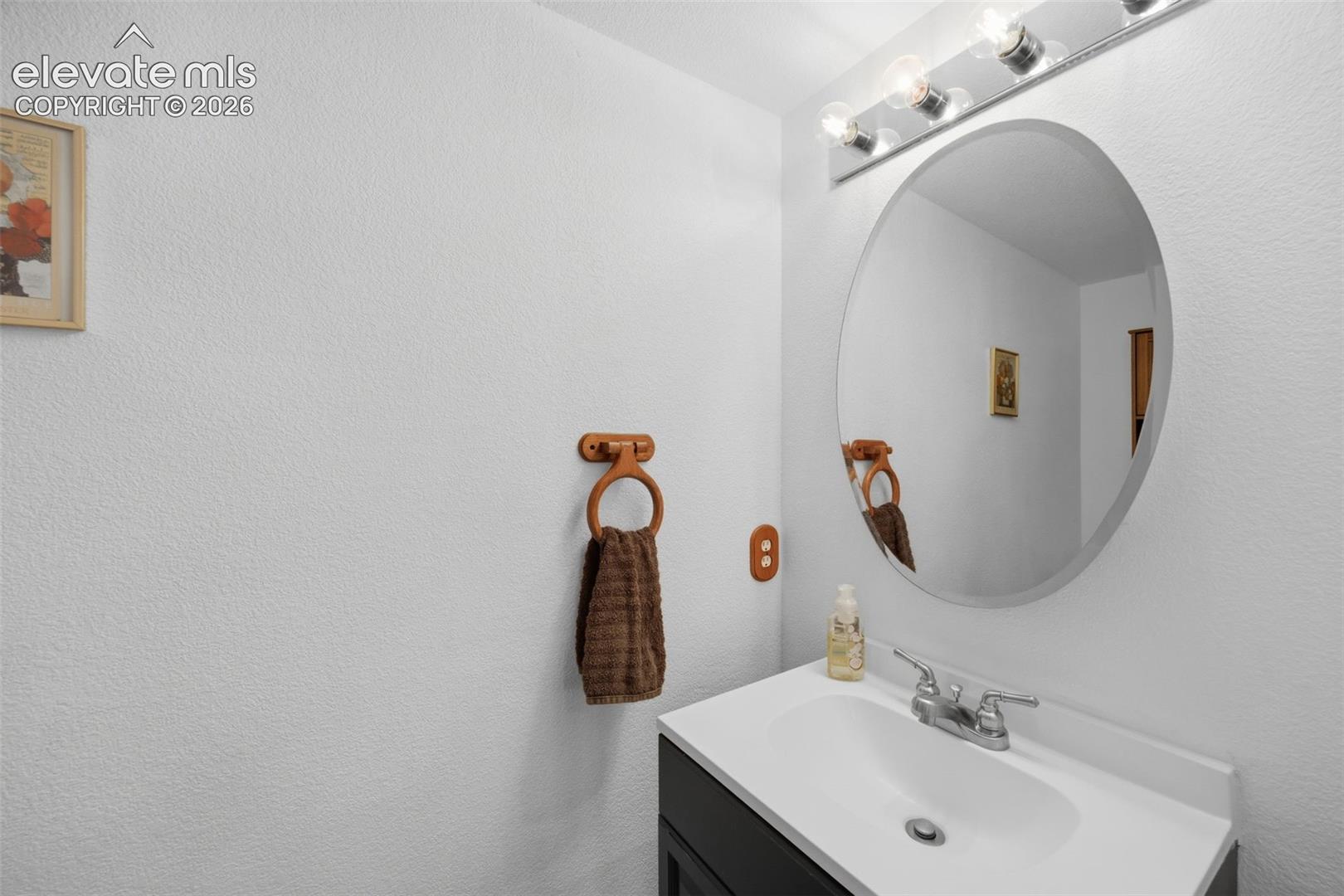 Bathroom vanity featuring a white countertop with integrated sink, chrome faucet, and dark wood-finish cabinetry