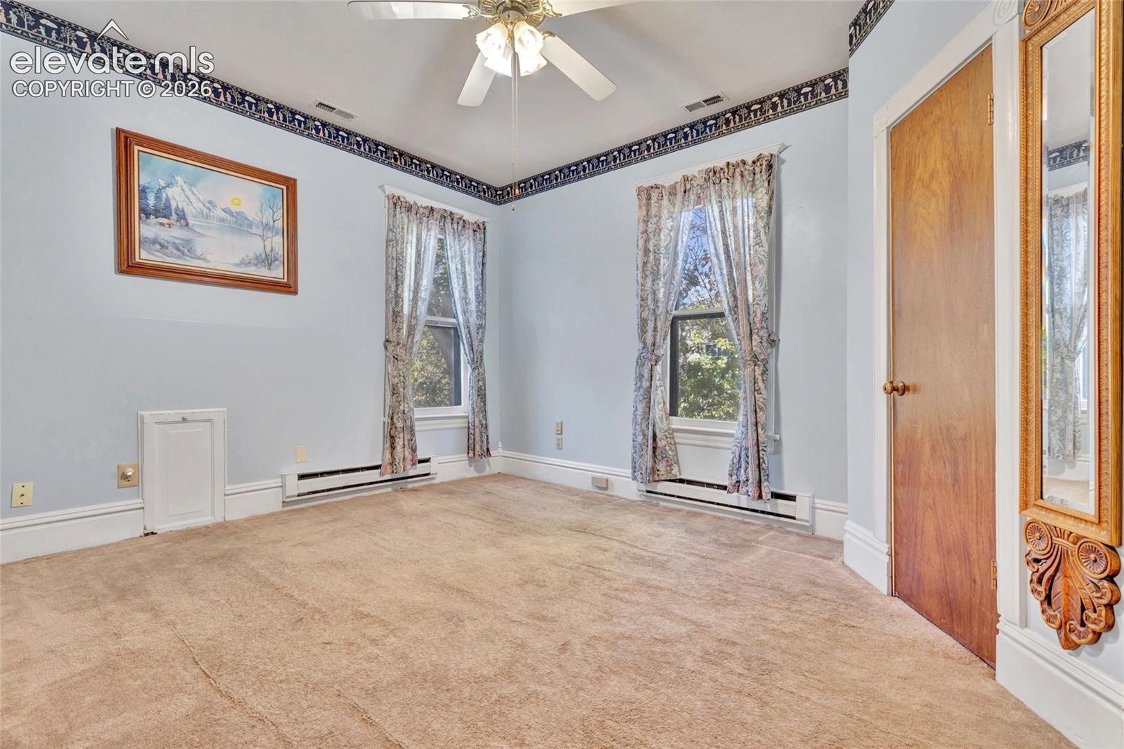 Interior room featuring wall-to-wall carpeting, a ceiling fan with integrated lighting, dual windows, and a wood-finish interior door