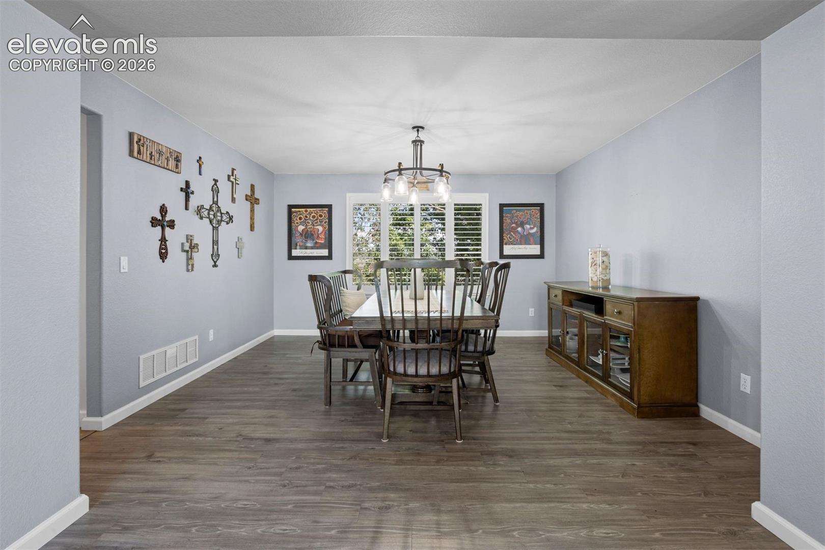 Spacious room featuring vinyl flooring, a contemporary chandelier, and window shutters