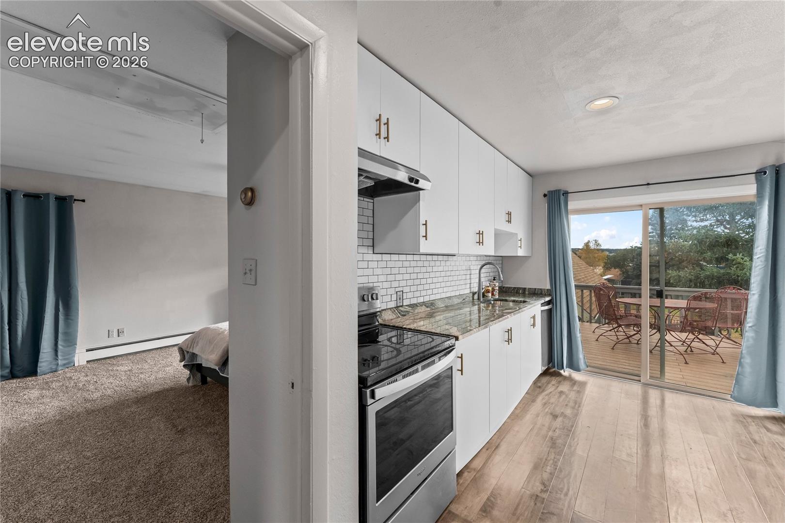 Kitchen featuring white flat-panel cabinetry, stone-finish countertops, a subway tile backsplash, stainless steel appliances, and wood-finish flooring