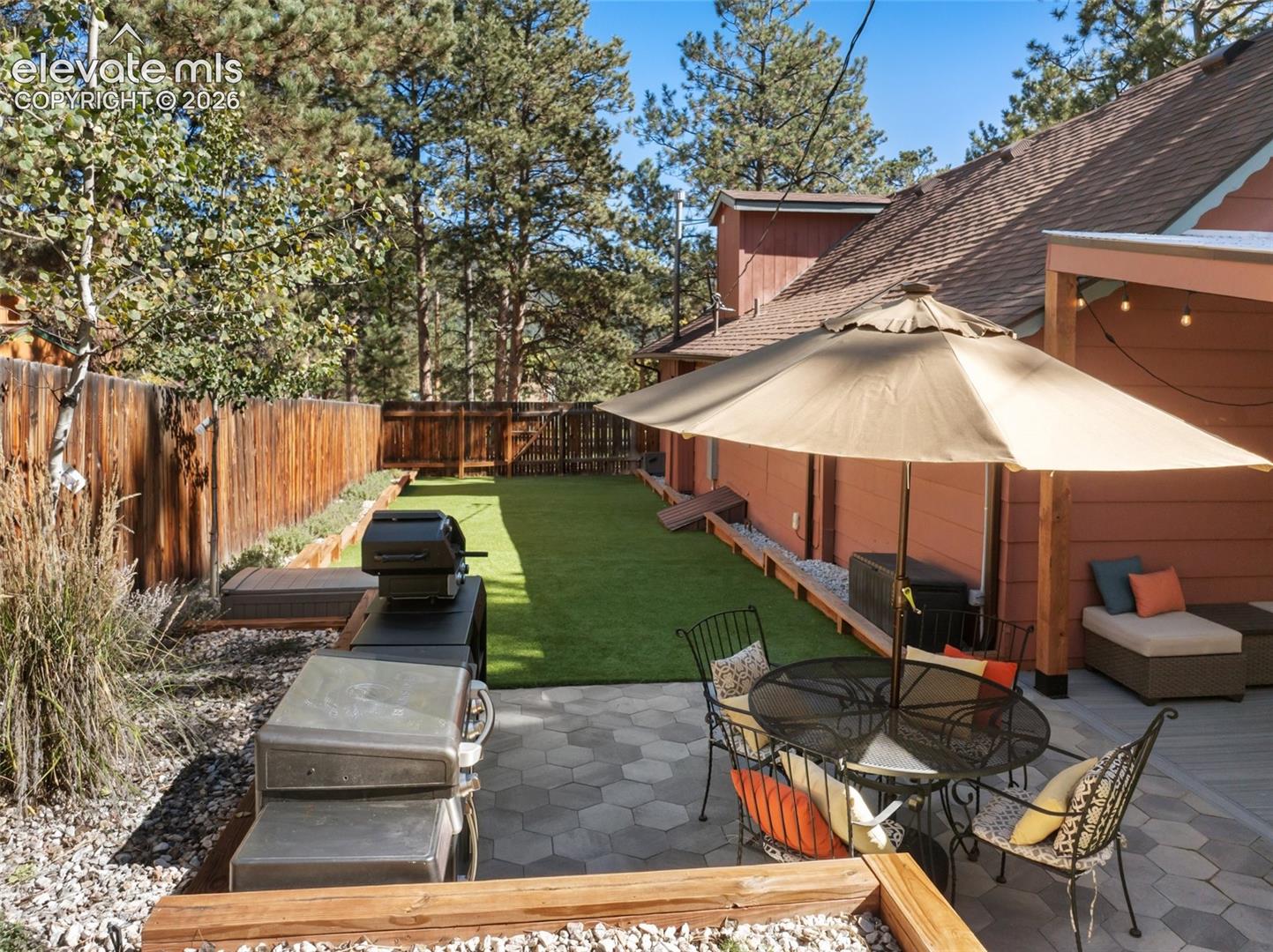 Backyard space featuring a hexagonal paver patio, synthetic turf lawn, wood privacy fencing, and a covered deck area