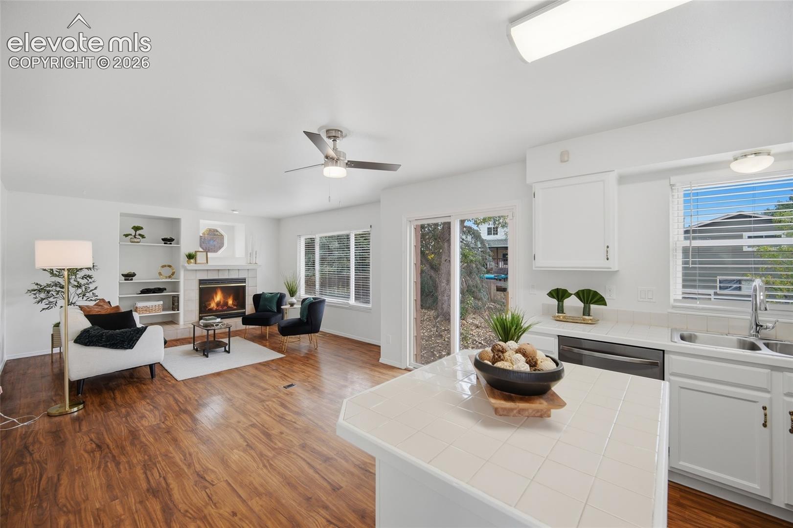 Open-concept interior featuring wood-finish flooring, a kitchen island with tile countertops, a built-in fireplace, and custom shelving