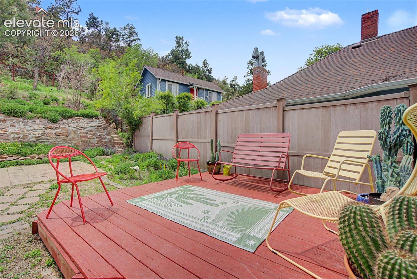 Outdoor wood deck with red finish, surrounded by a wood privacy fence and natural rock retaining wall