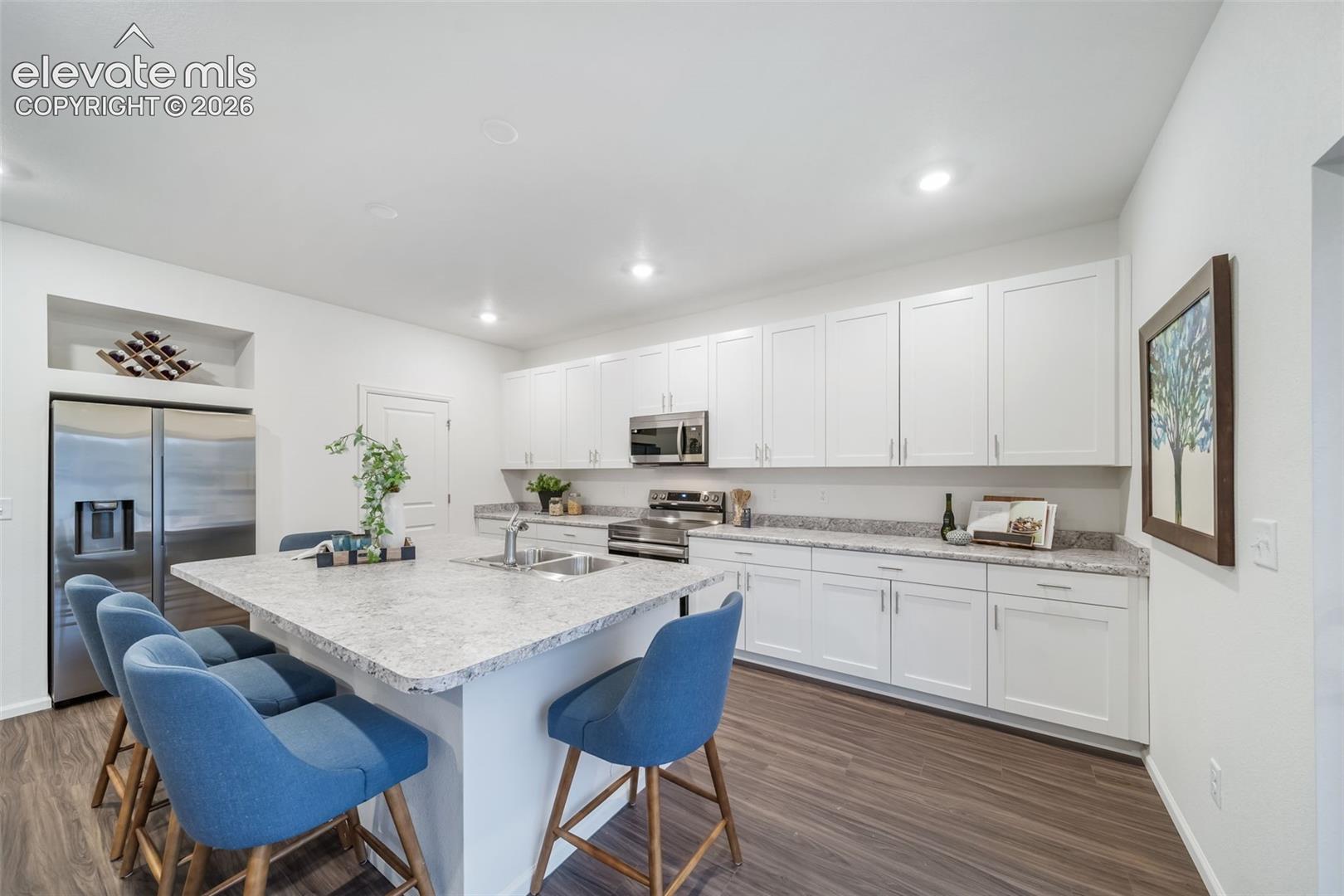 Kitchen featuring a central island with an undermount sink, stainless steel appliances, white cabinetry, and wood-finish flooring
*photos of a model home*