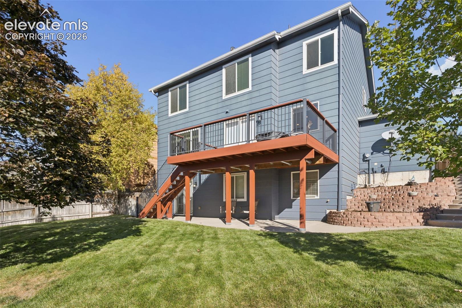Rear view with expanded covered patio, elevated deck with stairs and metal railings, and side yard concrete steps leading to front yard