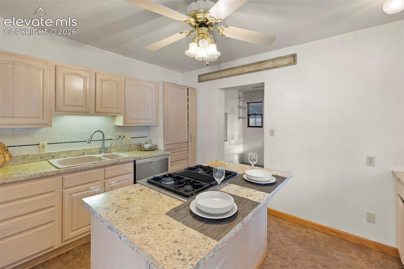 Kitchen featuring a center island with built-in cooktop, light-toned cabinetry, a double basin sink, and a ceiling fan