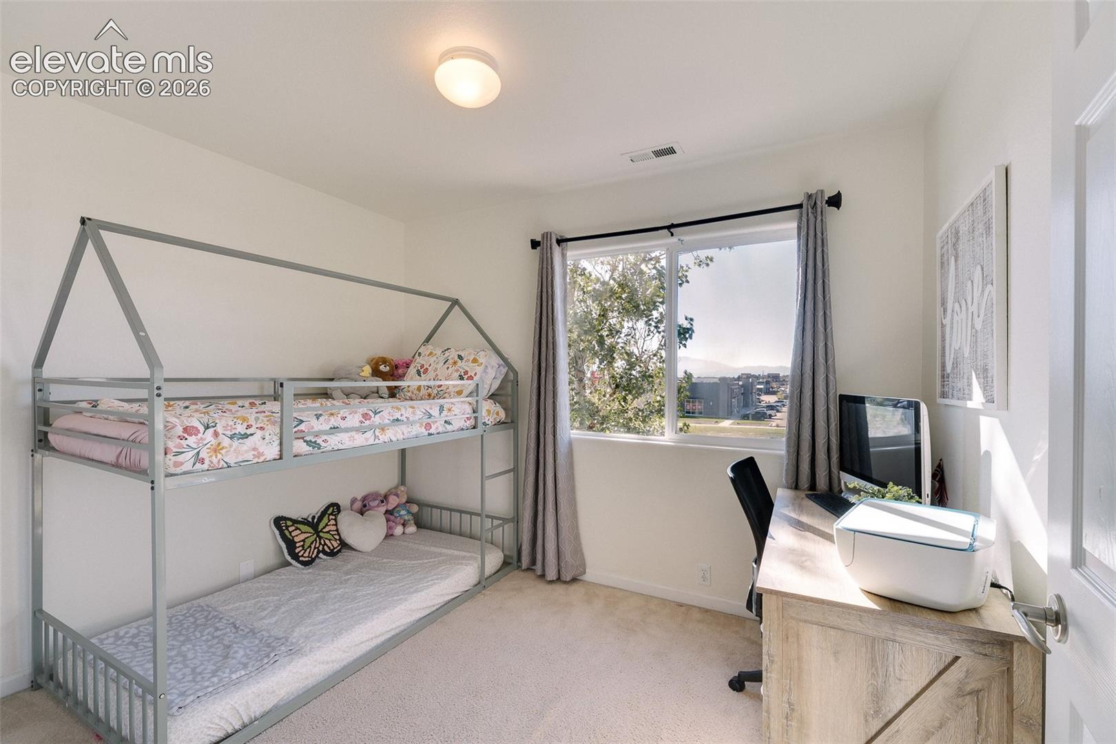 Recessed lighting, large window with outdoor scenery, light-toned carpeting, and a wood-finish desk