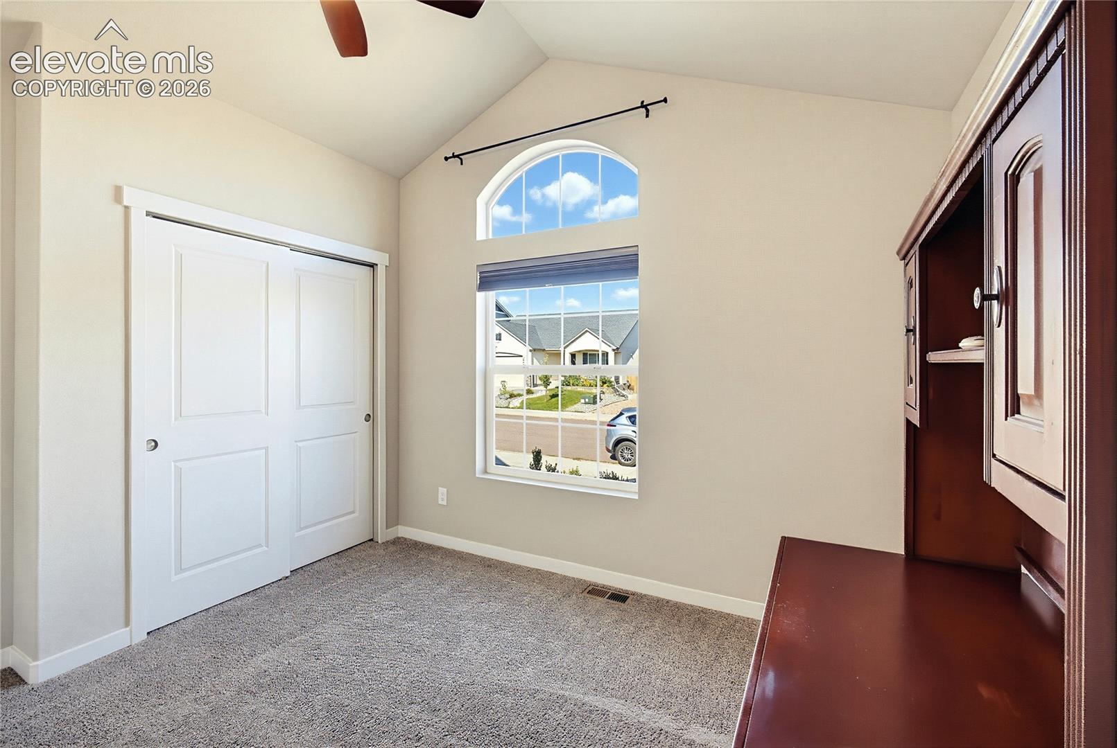 Vaulted ceilings featuring an arched window, neutral wall palette, carpeting, and double-panel sliding closet doors