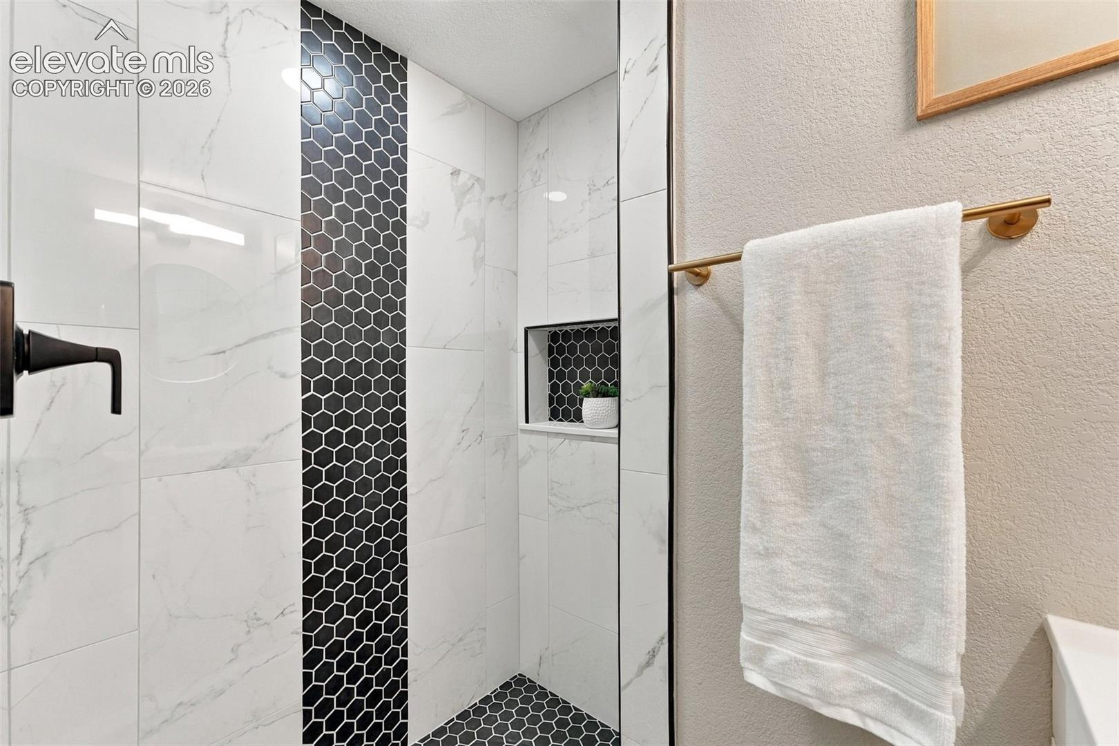 Walk-in shower featuring large-format white tile, a black hexagonal tile accent stripe, recessed shower niche, and matte black plumbing fixtures