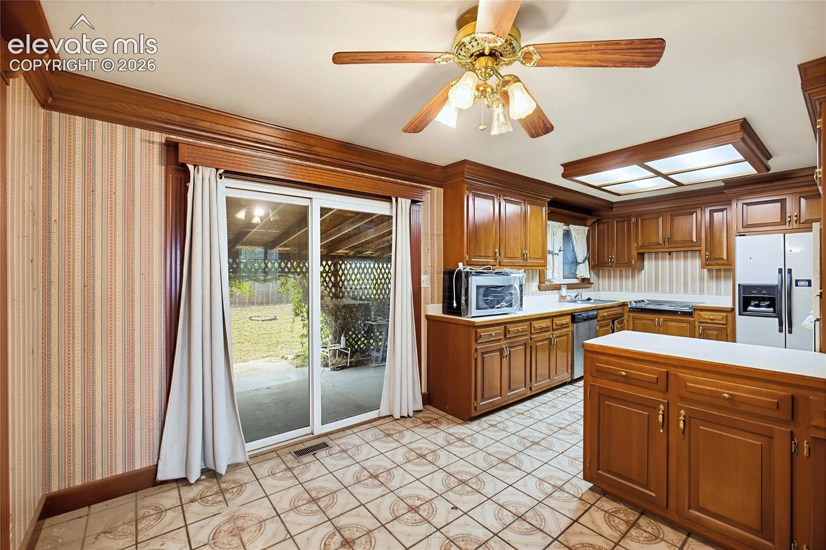 Kitchen featuring wood cabinetry, a center island, tile flooring, and a ceiling fan with integrated lighting
