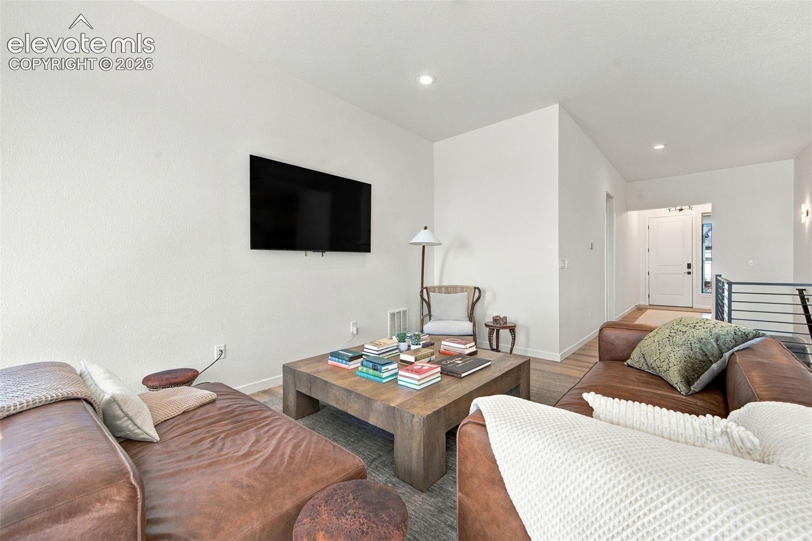 Neutral-toned living space featuring recessed ceiling lighting, wood-finish flooring, and a wall-mounted television bracket