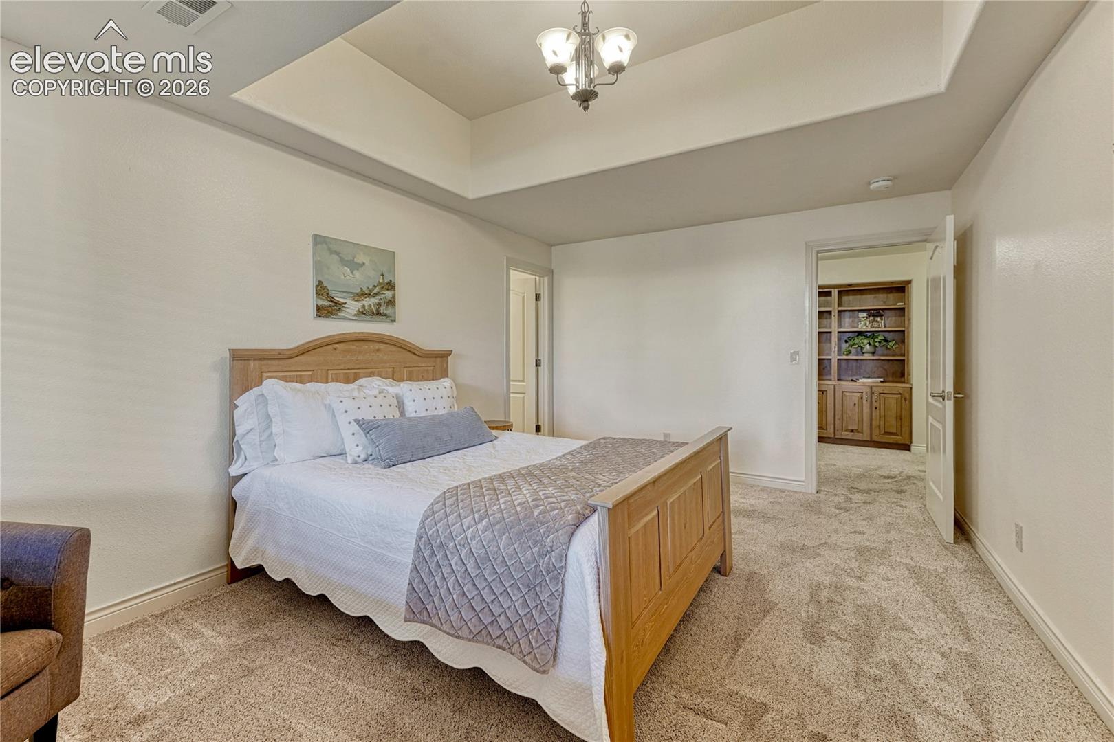 Tray ceiling with a central multi-light fixture, neutral carpeting, and built-in wooden cabinetry