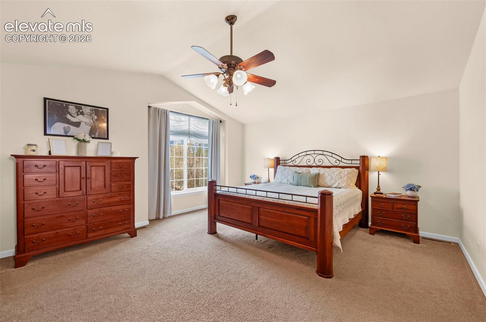 Spacious bedroom featuring vaulted ceilings, bay window, ceiling fan, and carpet flooring