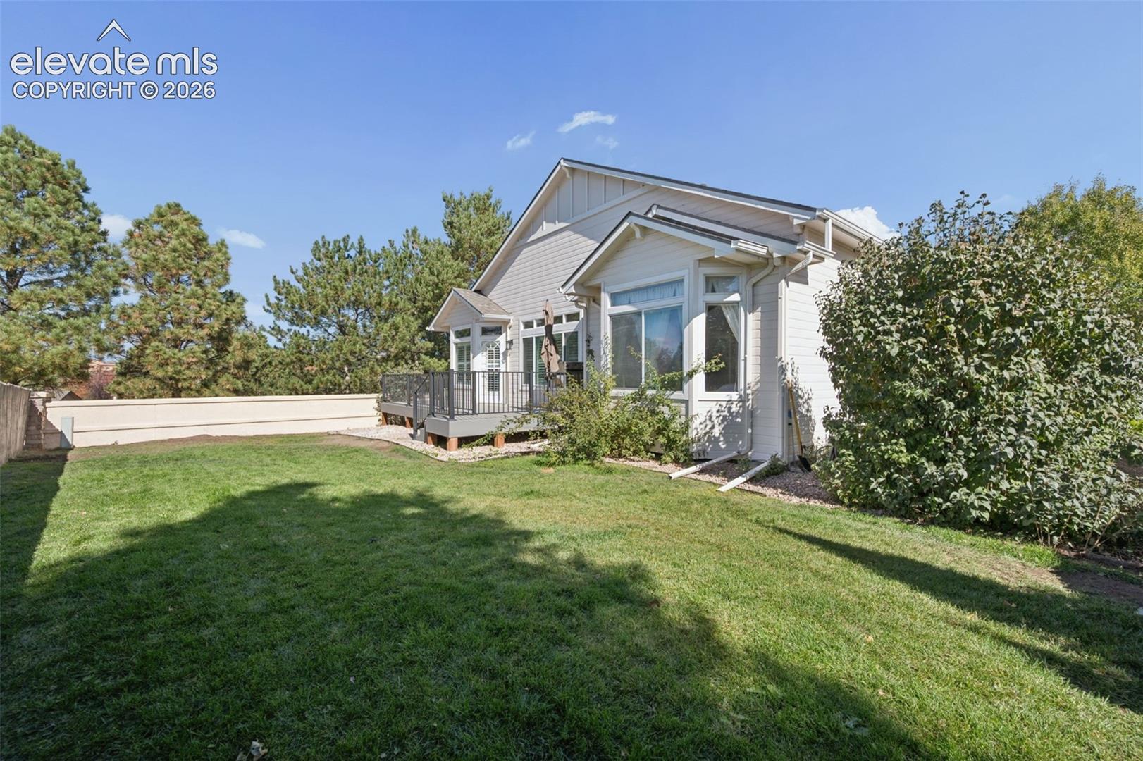 Backyard featuring a manicured lawn, elevated deck with iron railing, light-colored siding, bay windows, and perimeter privacy wall