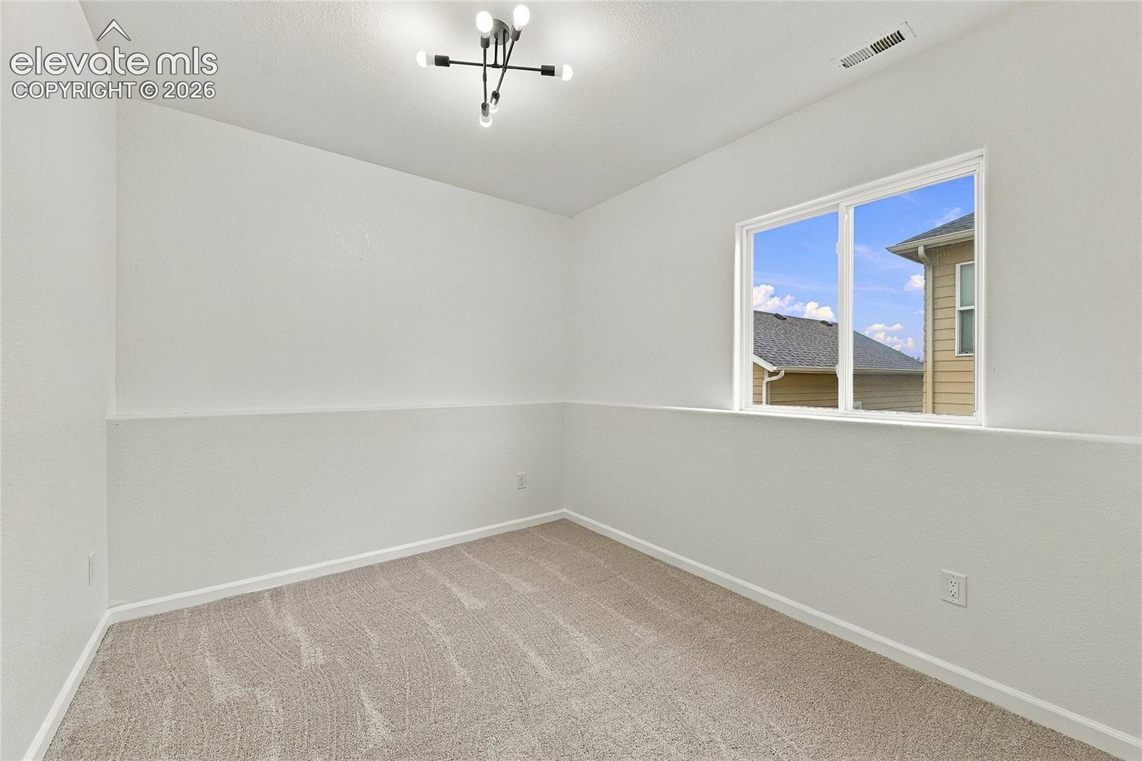 Interior space featuring neutral wall-to-wall carpeting, crisp white walls with chair rail molding, and a modern multi-arm sputnik-style overhead light fixture