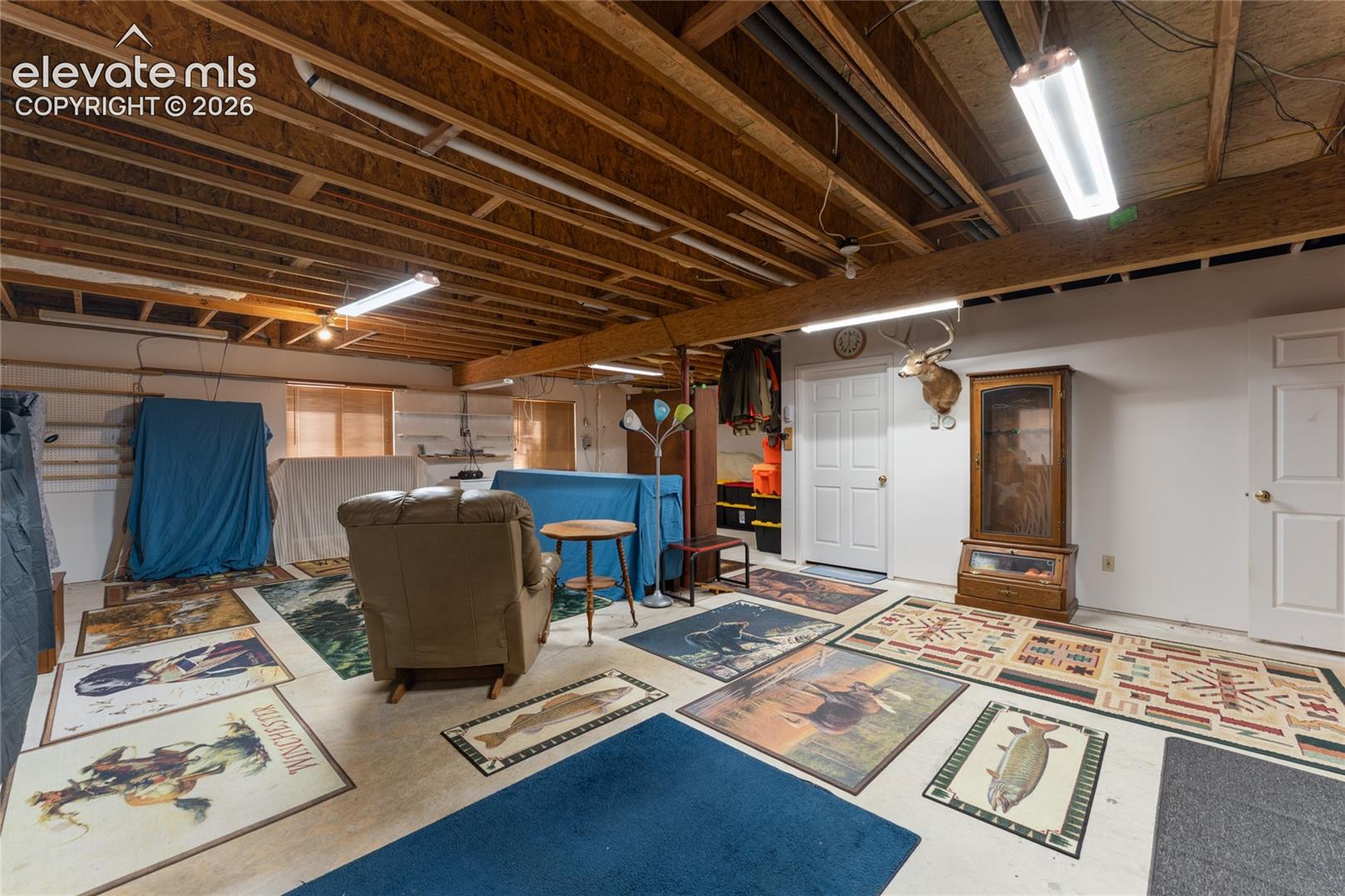 Spacious lower level with exposed ceiling joists and fluorescent lighting