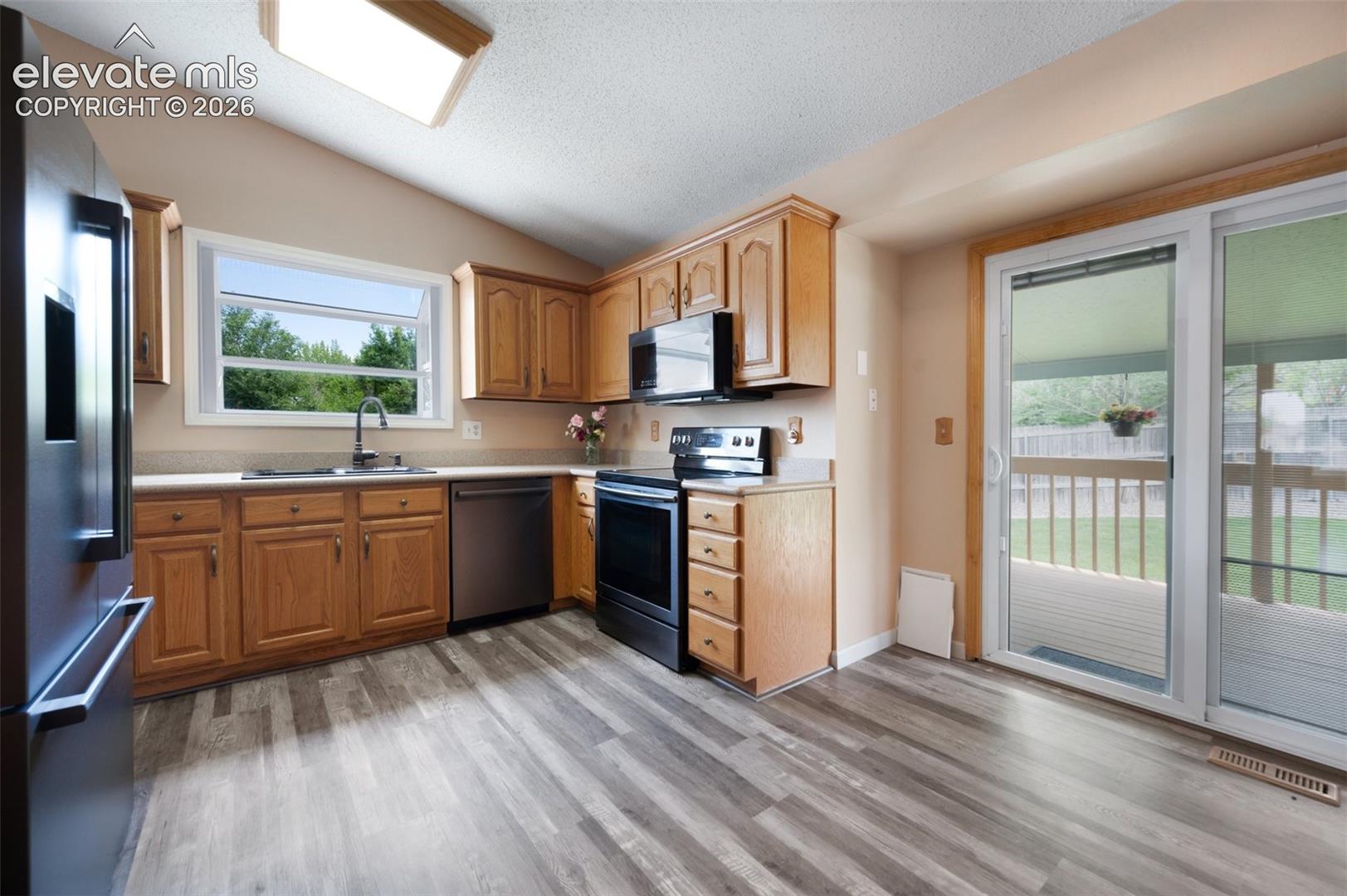 Kitchen with stainless steel appliances, a sink, vaulted ceiling, light countertops, and light wood-style flooring