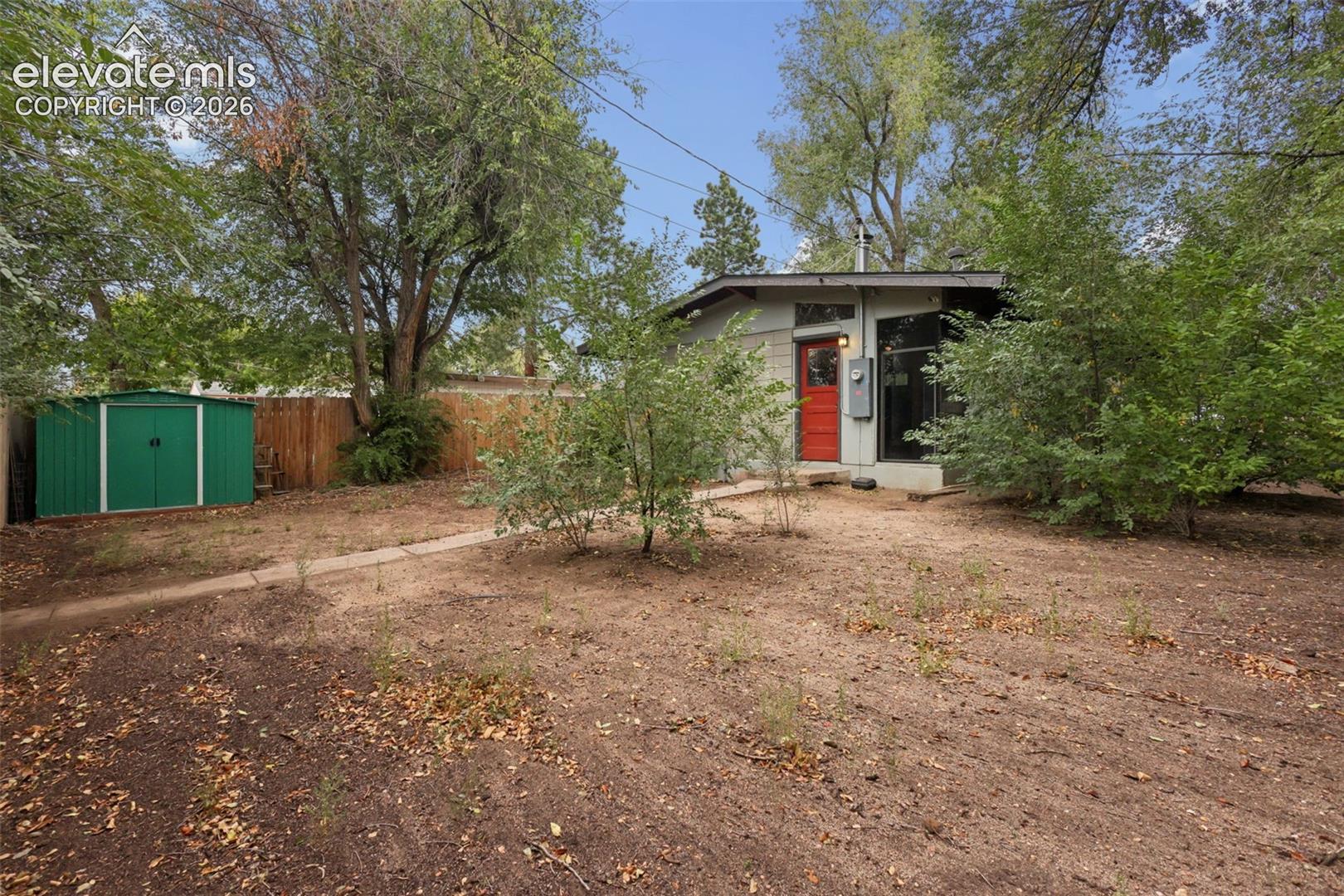 Exterior featuring a red entry door, a detached green storage shed, and a privacy fence
