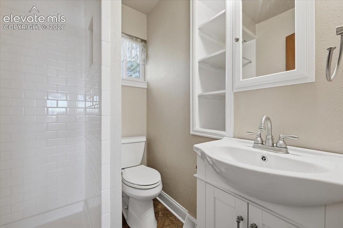 Bathroom featuring a subway-tiled shower surround, a white vanity cabinet with an integrated sink, a brushed nickel faucet, and built-in recessed shelving