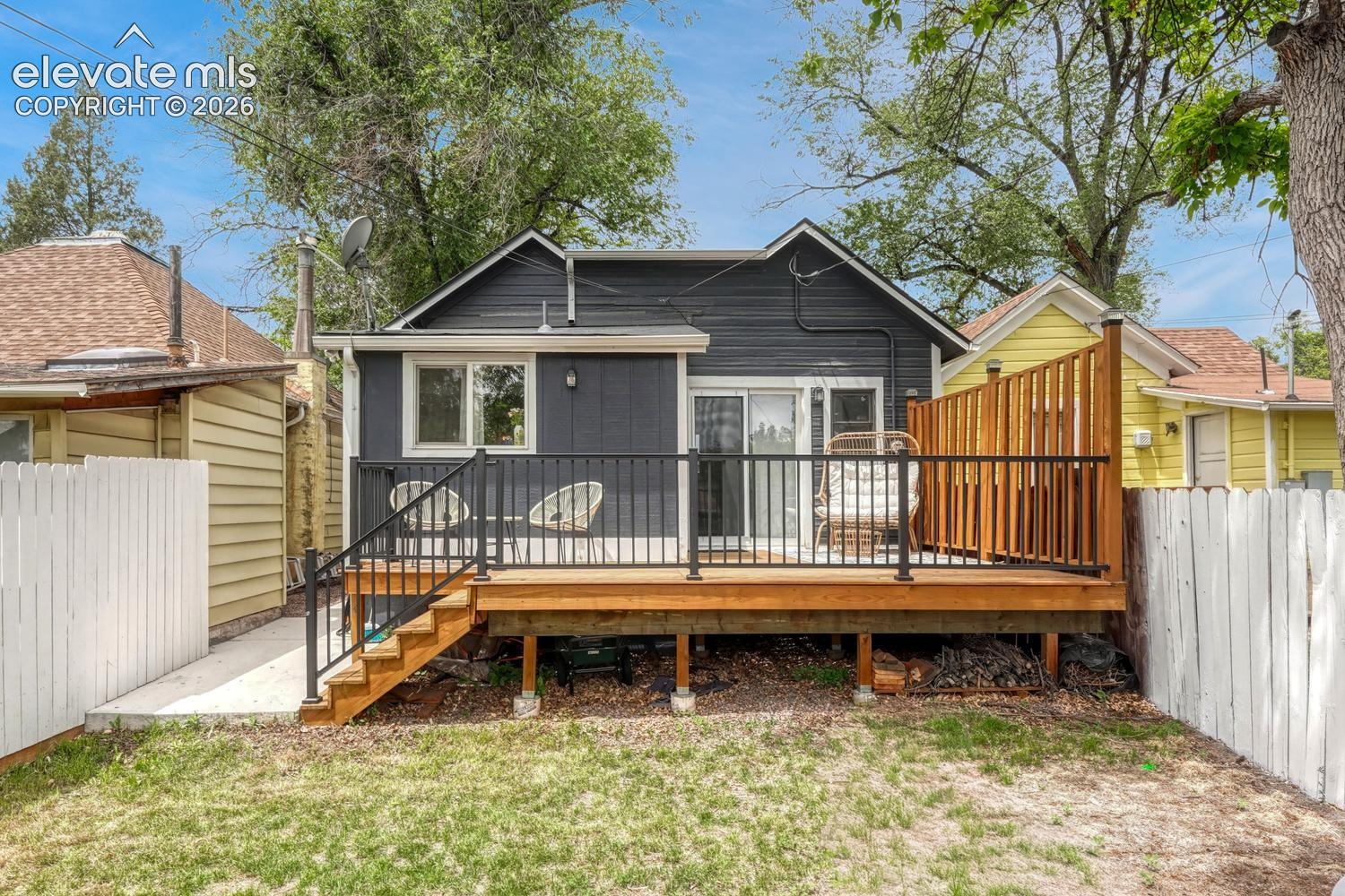 Rear exterior featuring a wood deck with black metal railings, wood privacy screen, and concrete pathway