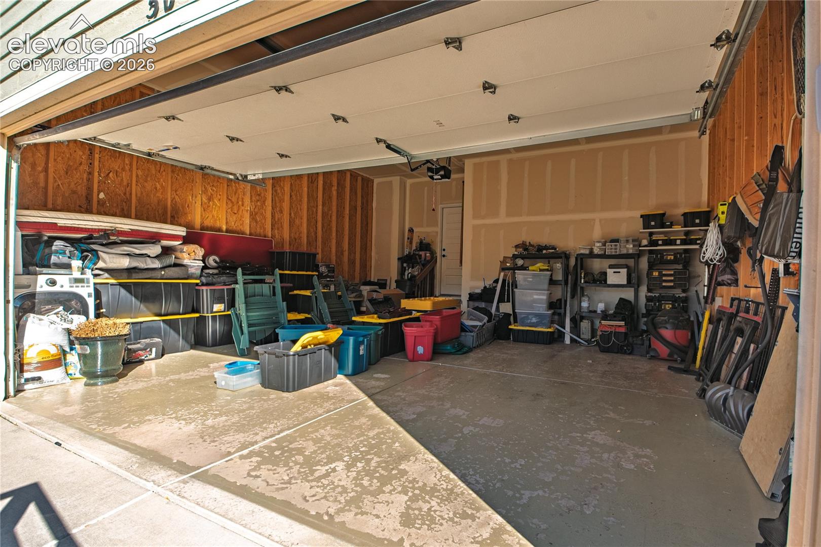 Multi-car garage featuring a concrete floor, overhead door, exposed wall studs, and interior access door