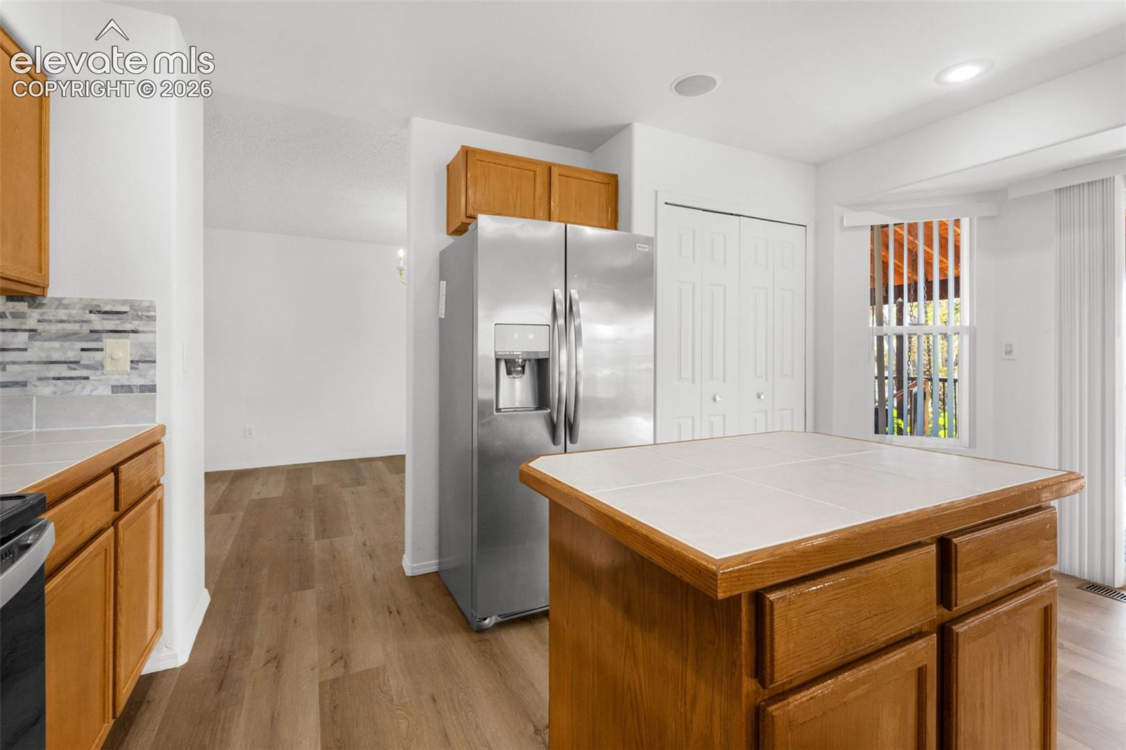 Kitchen featuring a stainless steel French door refrigerator, wood cabinetry, tile backsplash, and a tiled island countertop