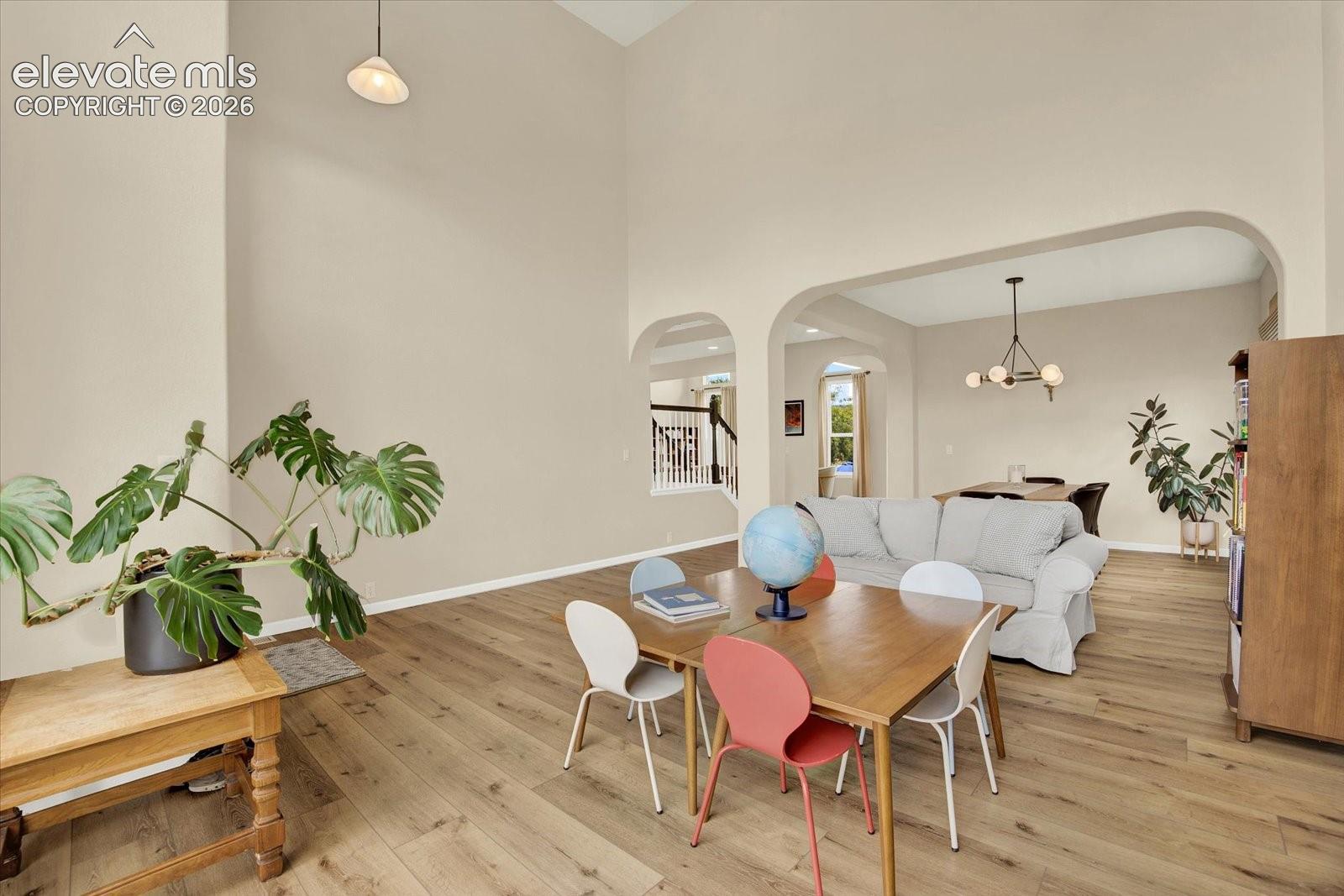 Expansive ceiling height, arched openings, and wood-finish flooring, featuring a pendant light fixture and a multi-arm chandelier