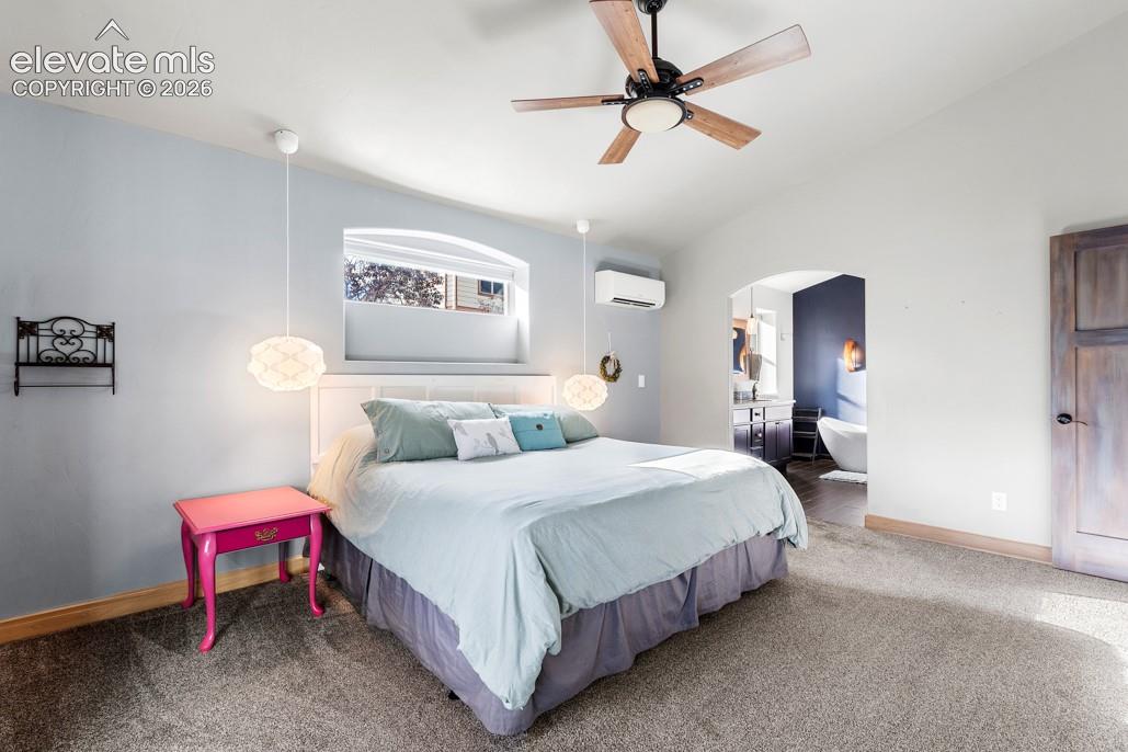 Vaulted ceiling with a wood-finish ceiling fan, recessed window alcove, and an arched doorway leading to a bathroom with a freestanding tub