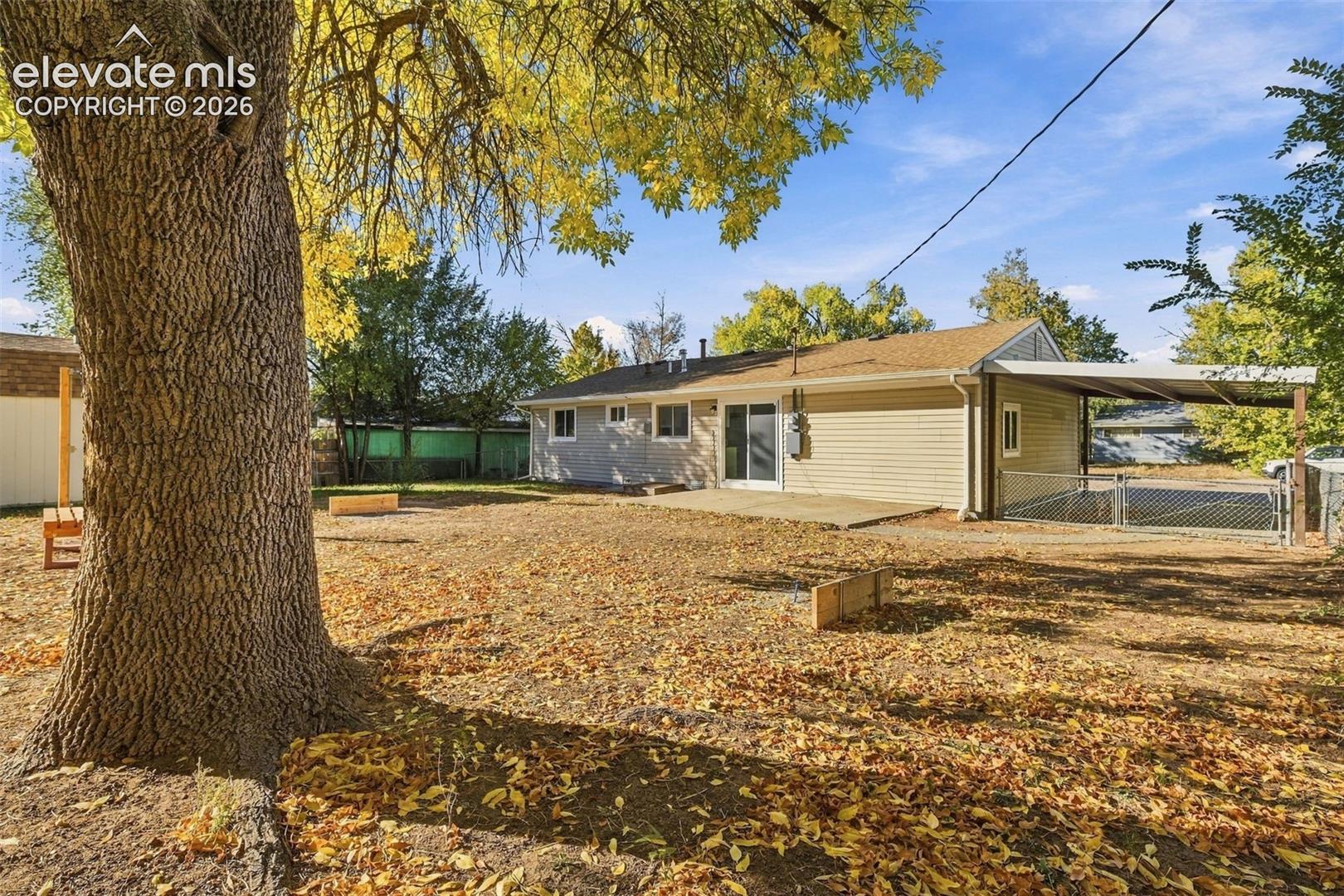 Rear exterior featuring horizontal lap siding, a concrete patio, an attached carport, and a chain-link fenced area