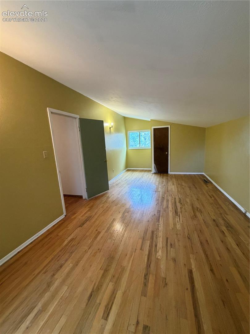 Interior space featuring wood-finish flooring, vaulted ceilings, and natural lighting from a wall-mounted window