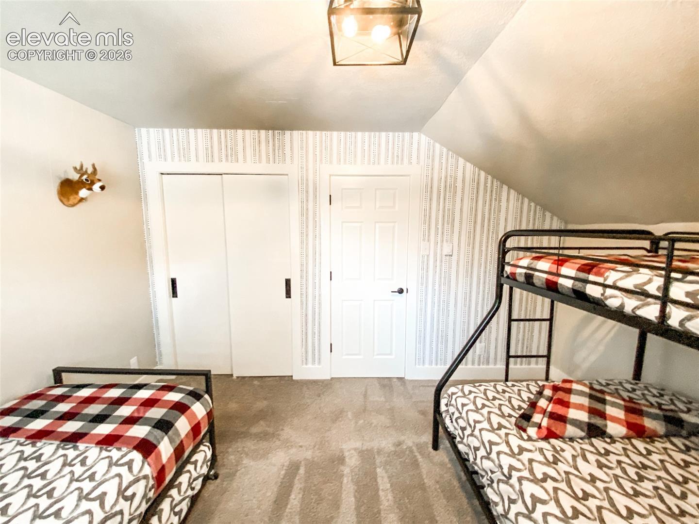 Carpeted room featuring a sloped ceiling, light-colored walls, and a patterned accent wall