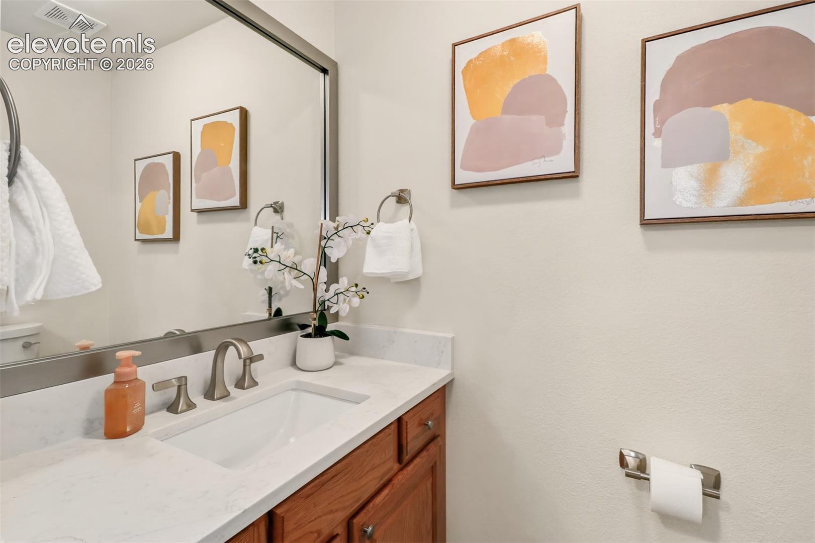 Wood-finish cabinetry paired with a light-toned stone-style countertop, an integrated rectangular undermount sink, a metallic-finish widespread faucet, and a large wall-mounted mirror