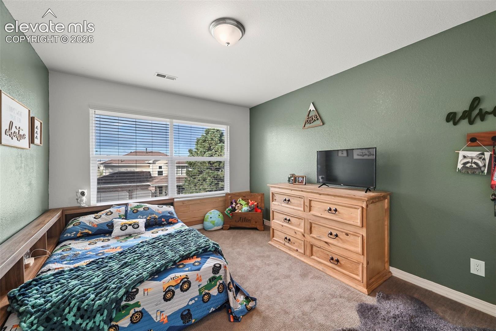 Recessed lighting, large window with horizontal blinds, built-in wooden bed frame, and textured carpeting
