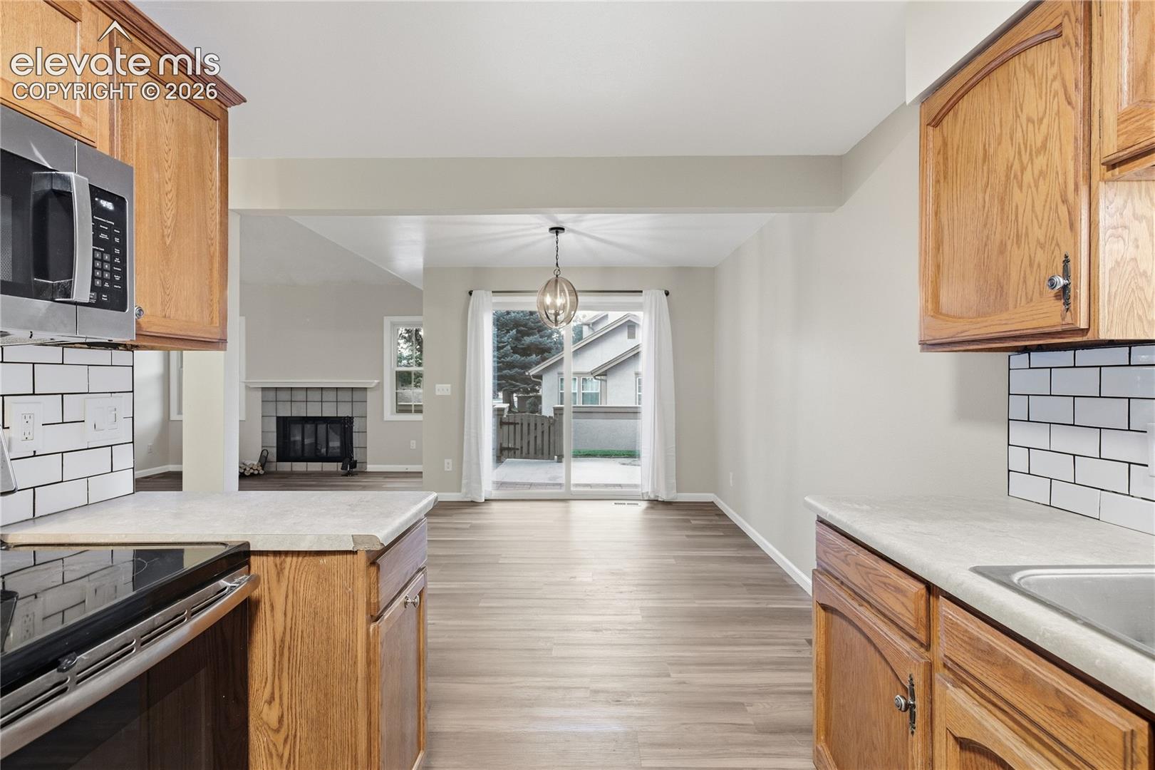 Wood-finish flooring throughout, stainless steel microwave, white subway tile backsplash, sliding glass door, and a built-in fireplace