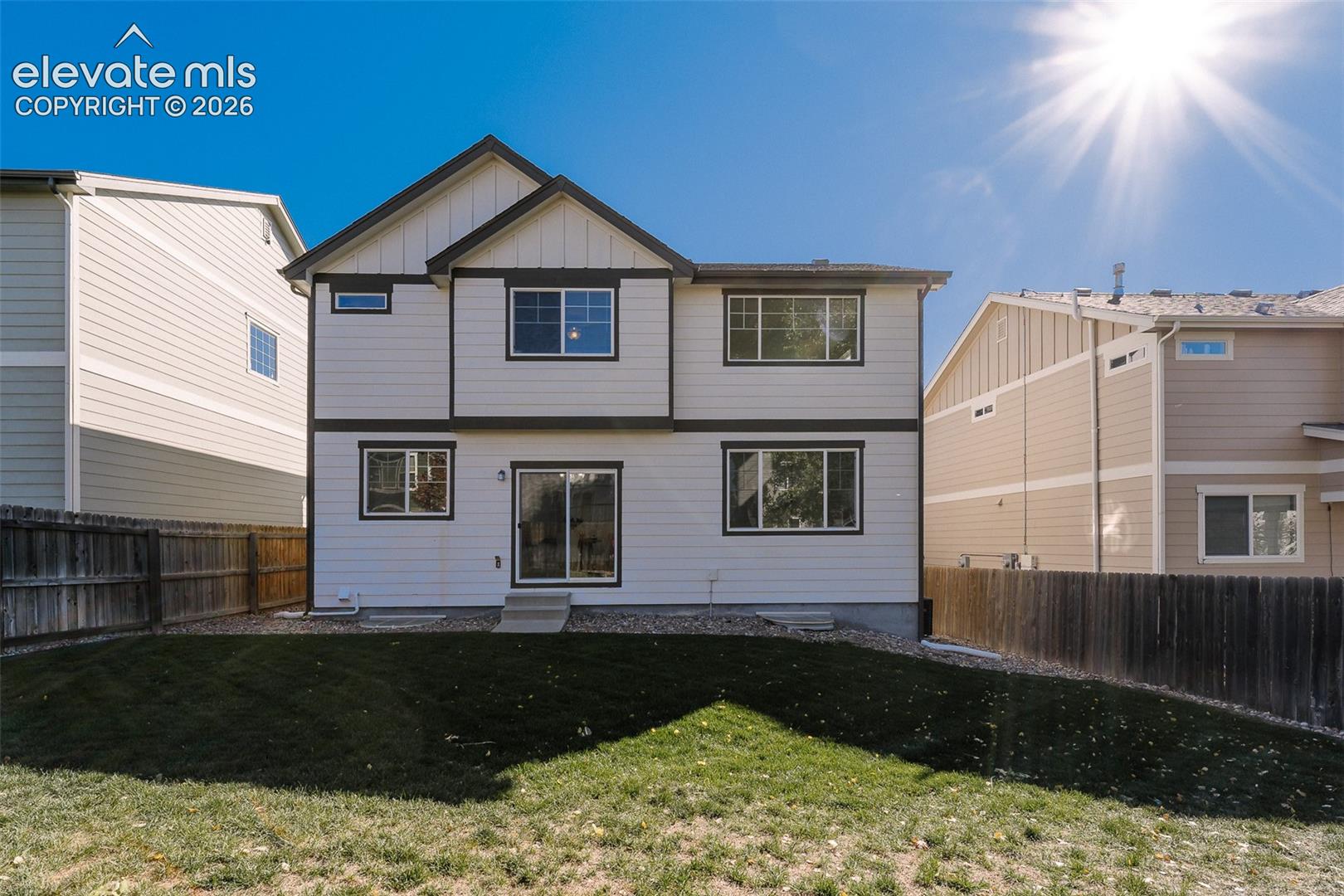 Two-story residence with horizontal siding, a gabled roofline, sliding glass door, and a fenced backyard