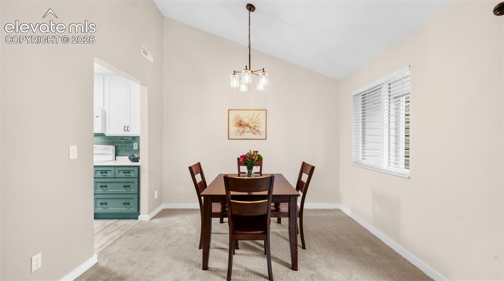 Dining area featuring vaulted ceilings, a contemporary chandelier, and a window with blinds